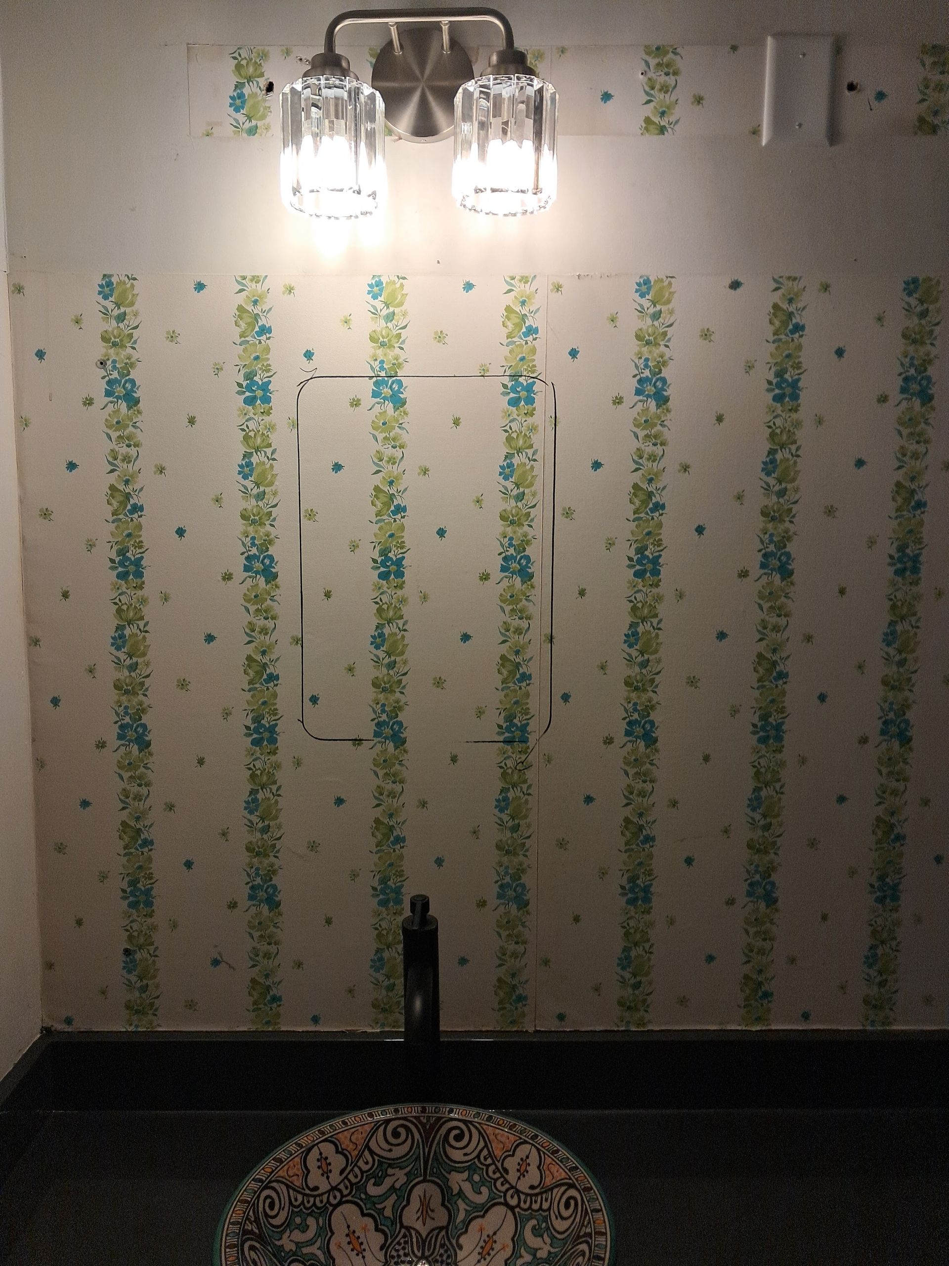 Bathroom wall with striped floral wallpaper, light fixture, and a dark sink.