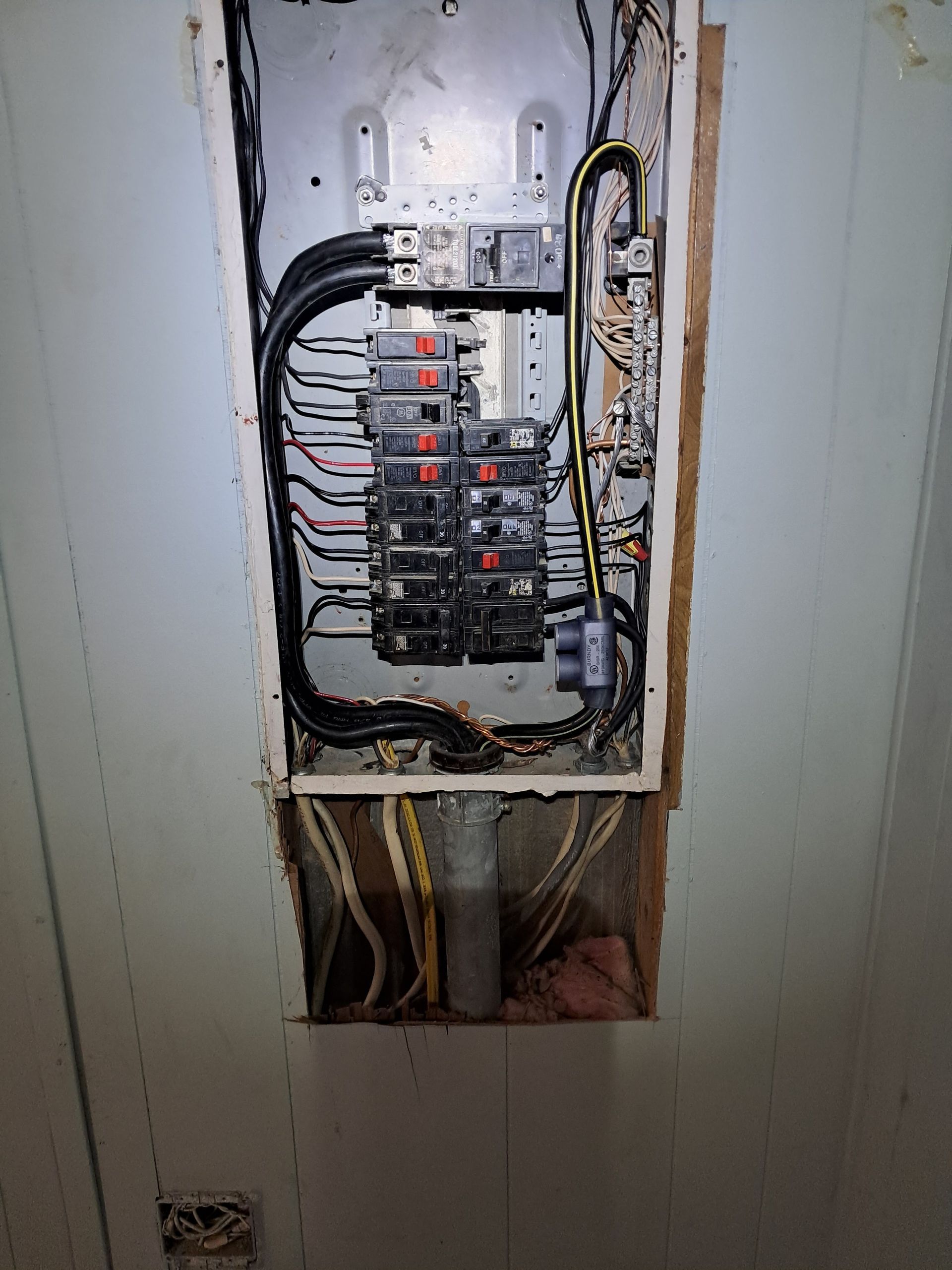 Open electrical panel with wires and breakers. Panel is in a wall cavity, with exposed wires.
