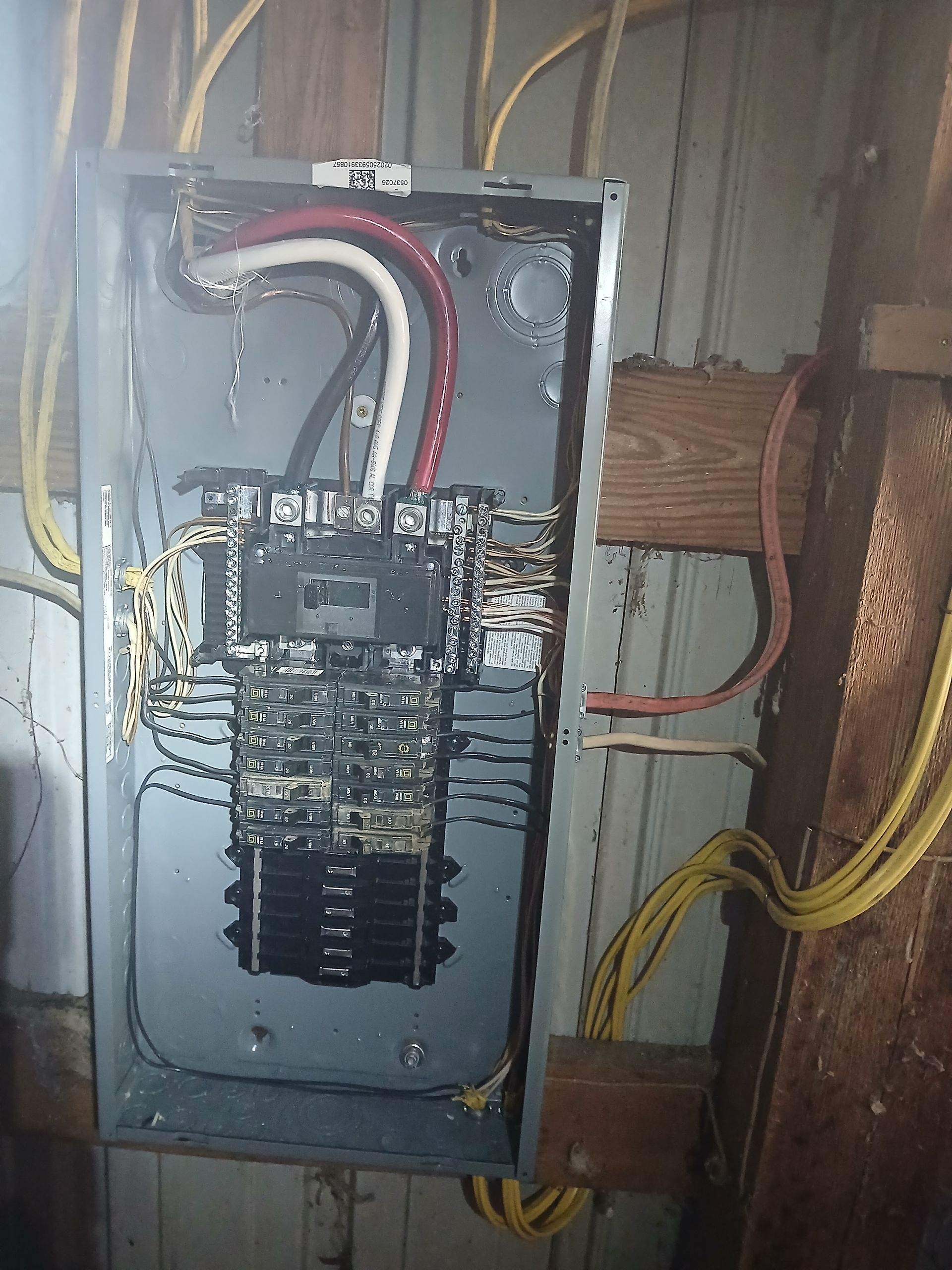 Electrical panel with multiple circuits and wiring, mounted on a wooden surface with yellow and red cables.