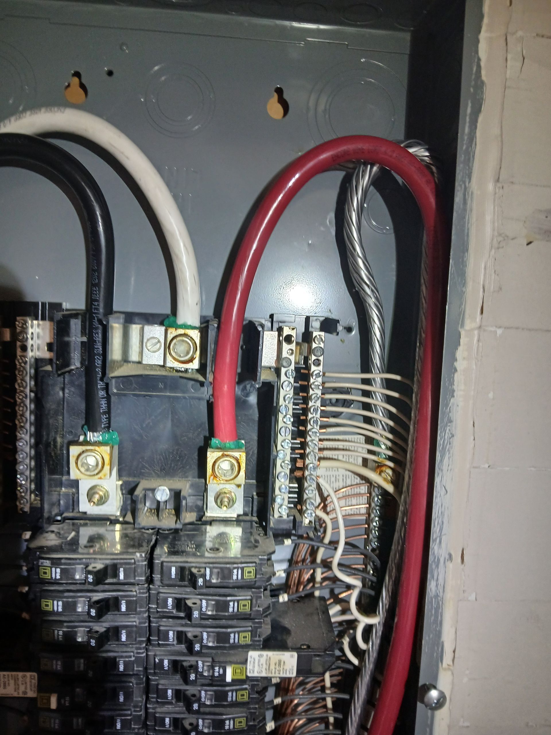 Electrical panel with black, white, and red wires connected to breakers and bus bars inside a metal enclosure.