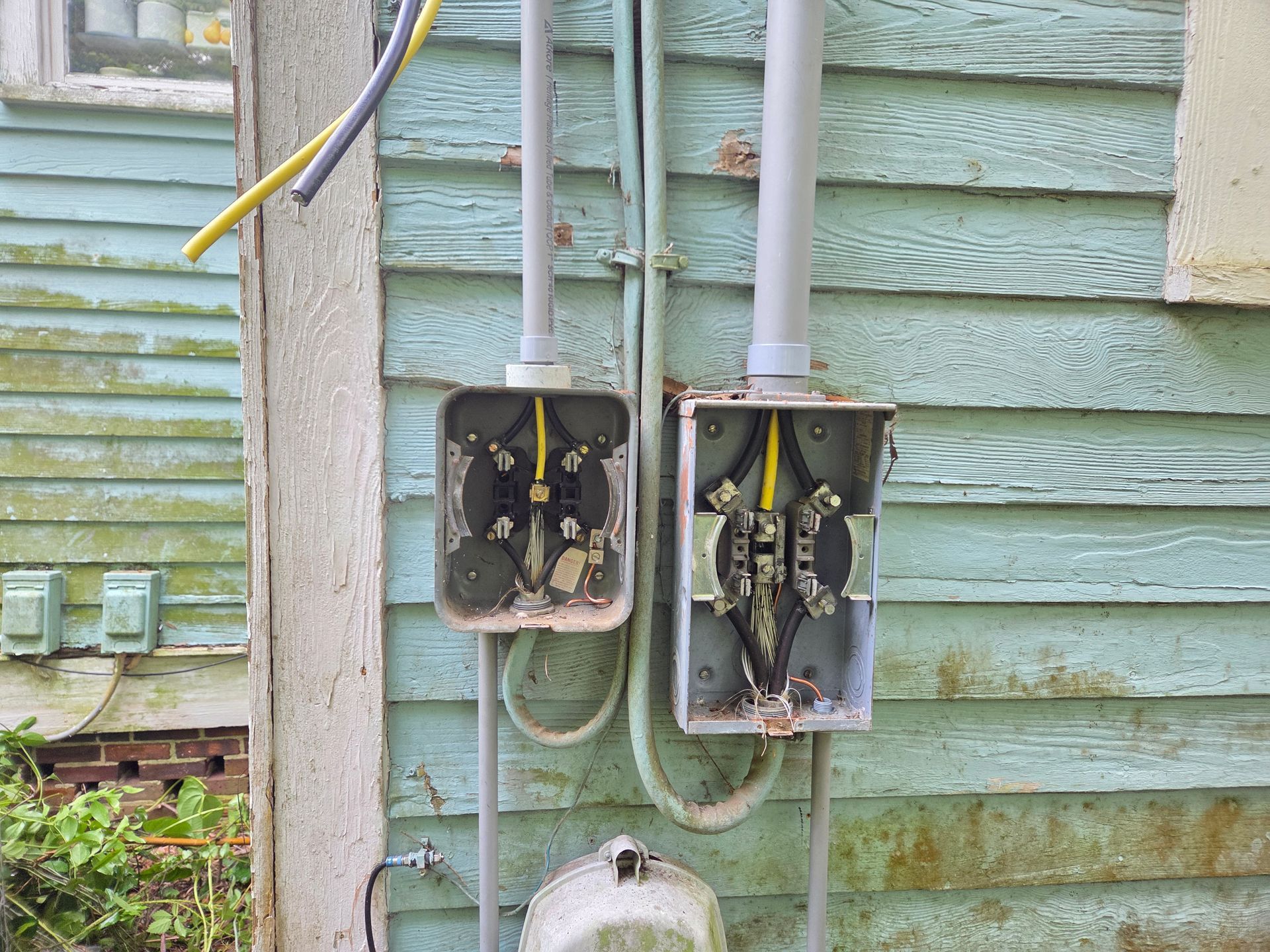 Two damaged electrical junction boxes on a weathered blue building exterior.