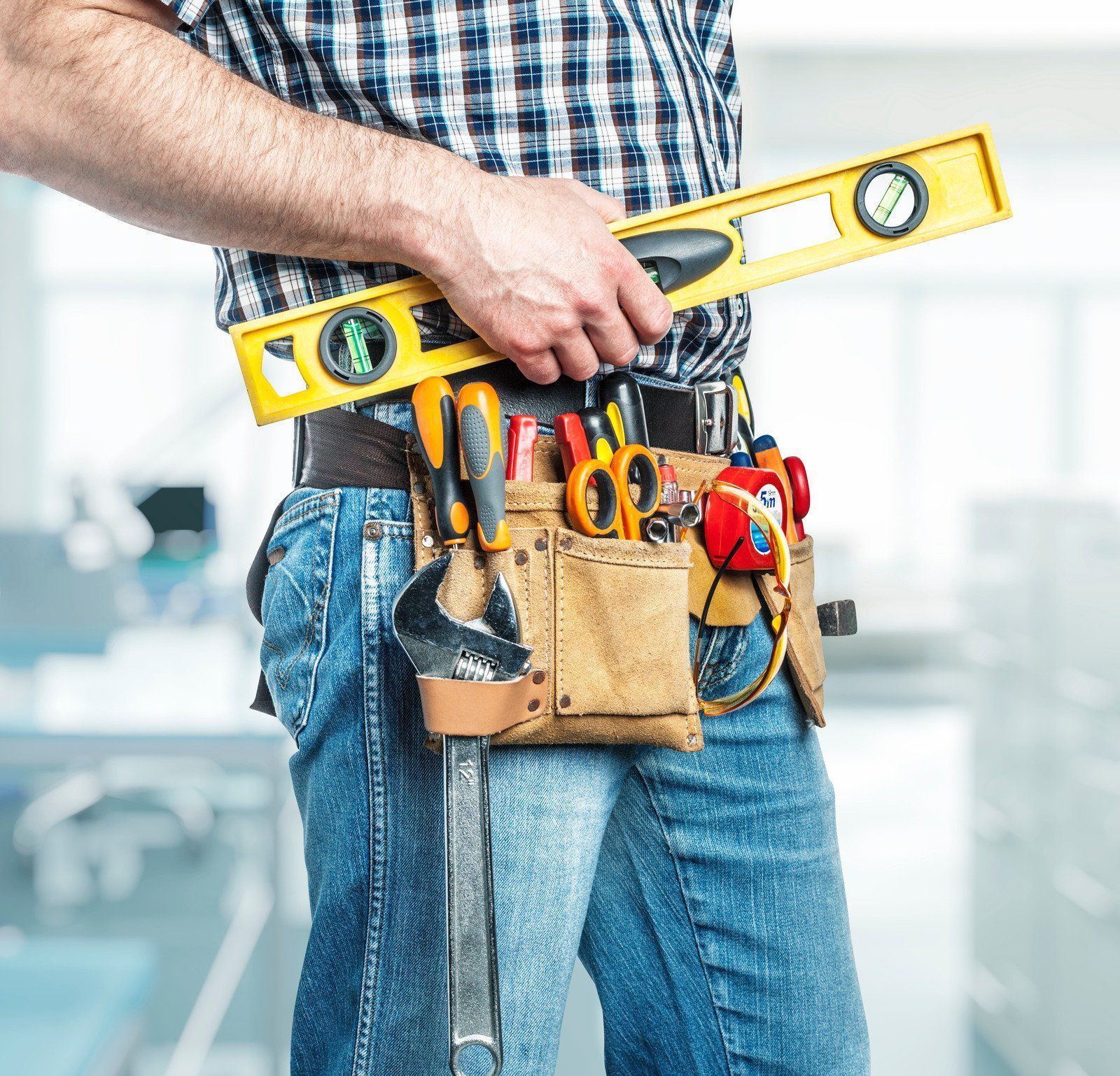 Person in blue jeans with a tool belt holding a yellow level.