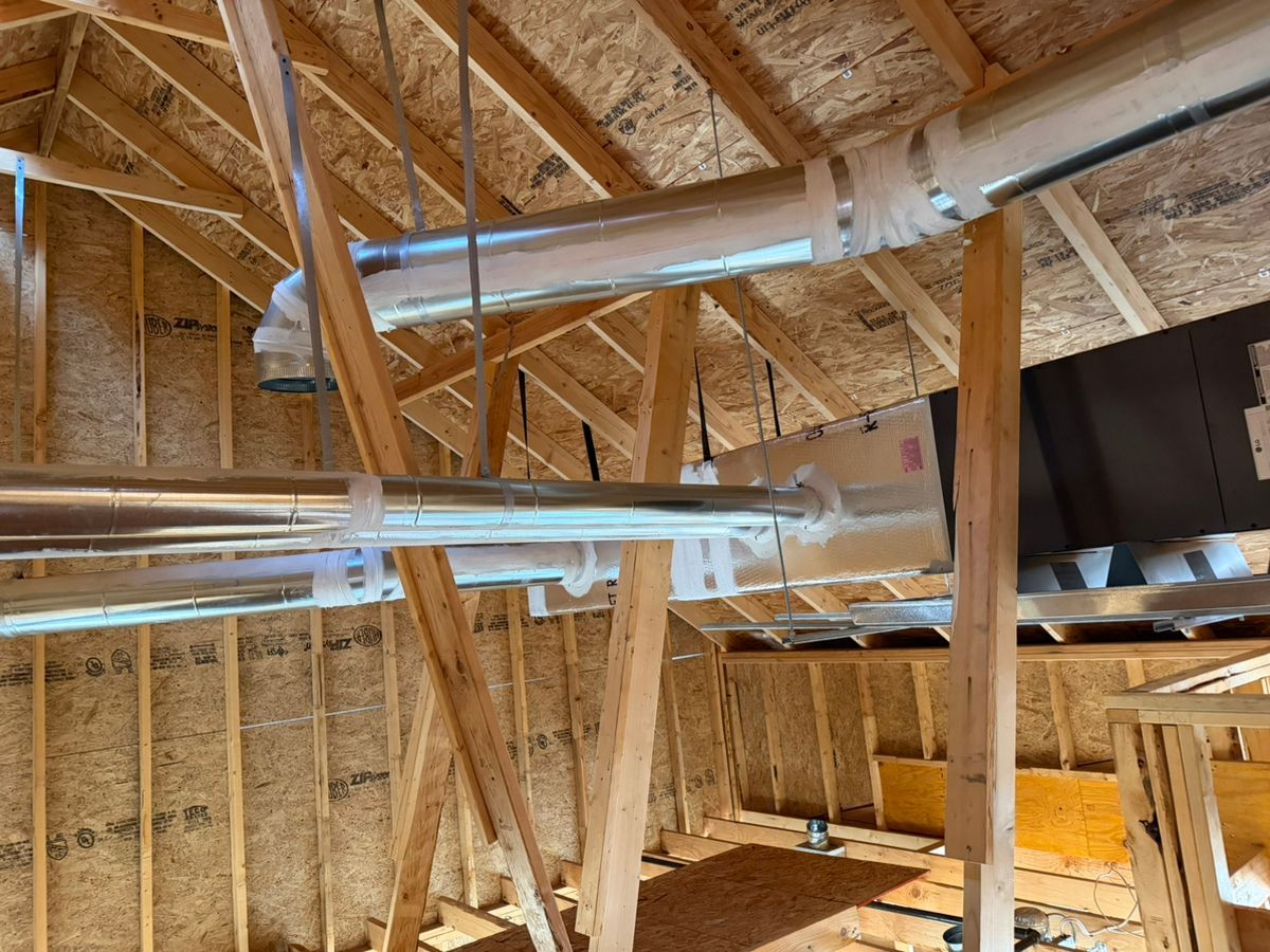Attic framing with exposed wooden rafters and shiny HVAC ducts under construction