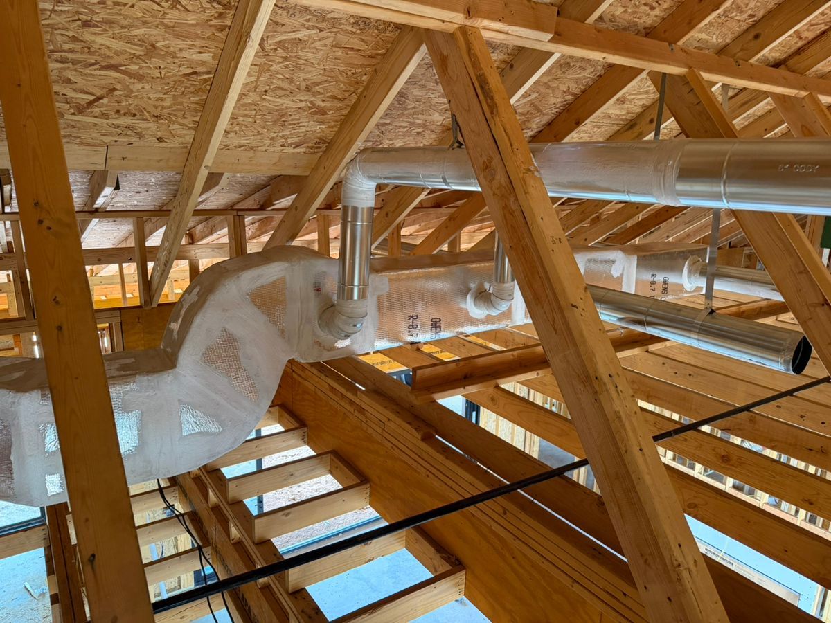 Attic construction with wooden roof trusses, silver HVAC ductwork, and skylight openings.