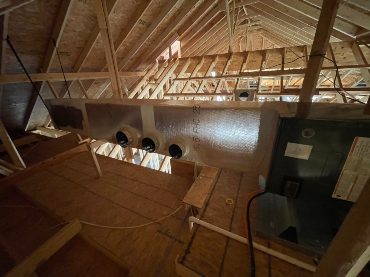 Attic under construction with exposed rafters, insulation, ducts, and a workbench in dim light