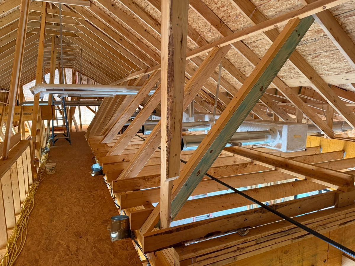 Unfinished attic framing with exposed wooden trusses and beams inside a construction site