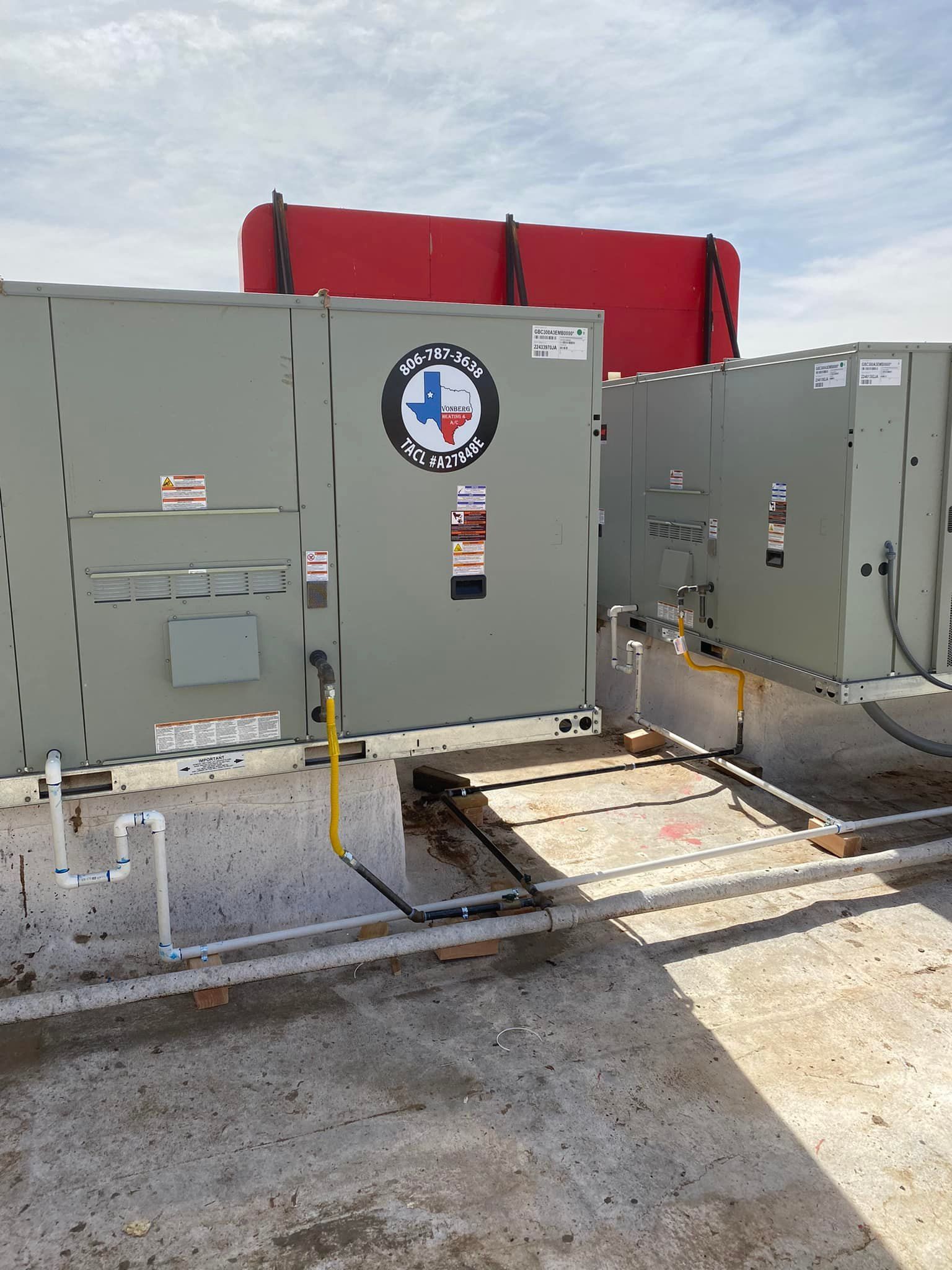 Gray rooftop electrical equipment with red cover, hazard markings, and open access panels on a gravel roof.