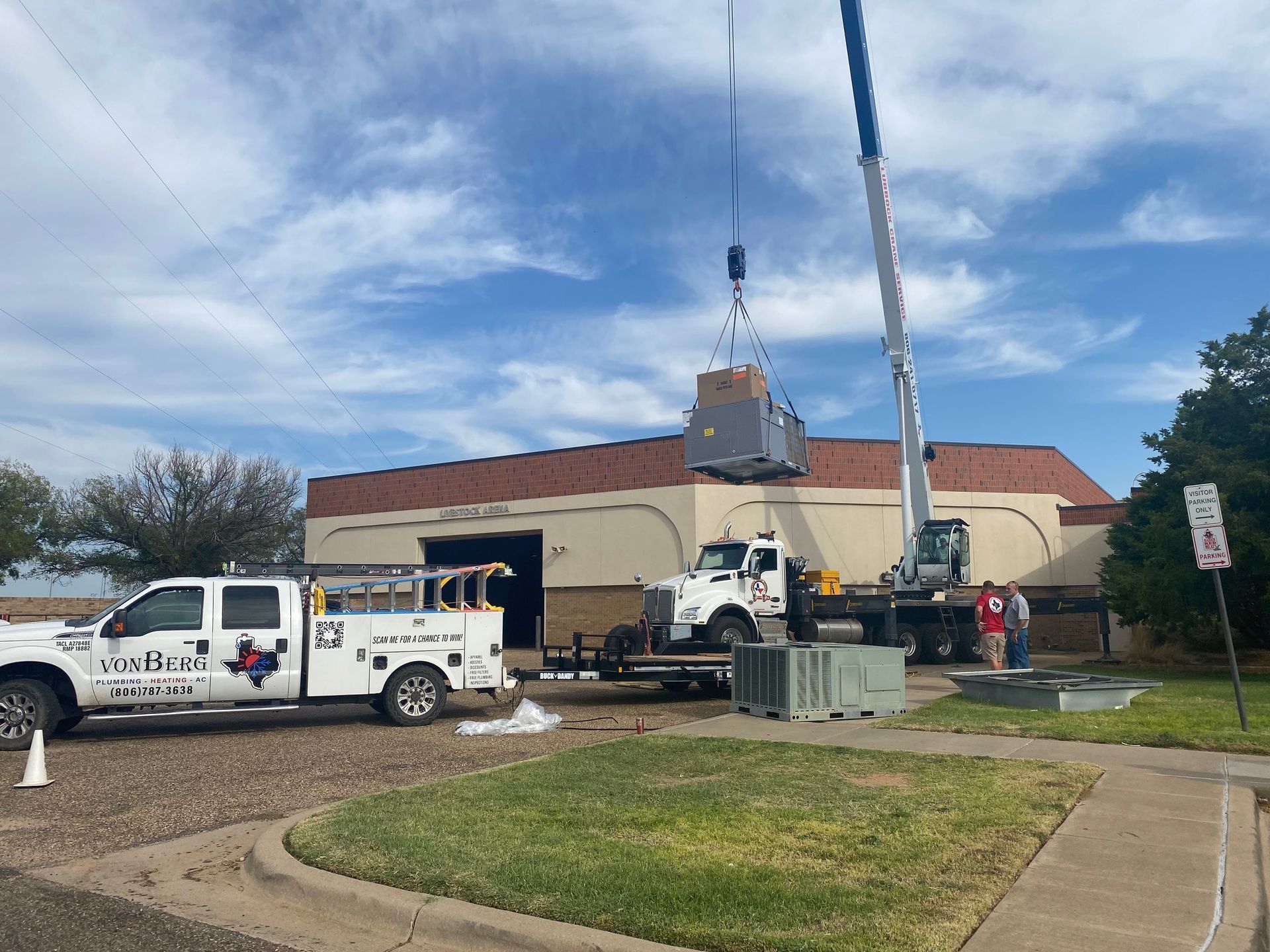 Crane lifting equipment to a building, with service trucks and workers present.