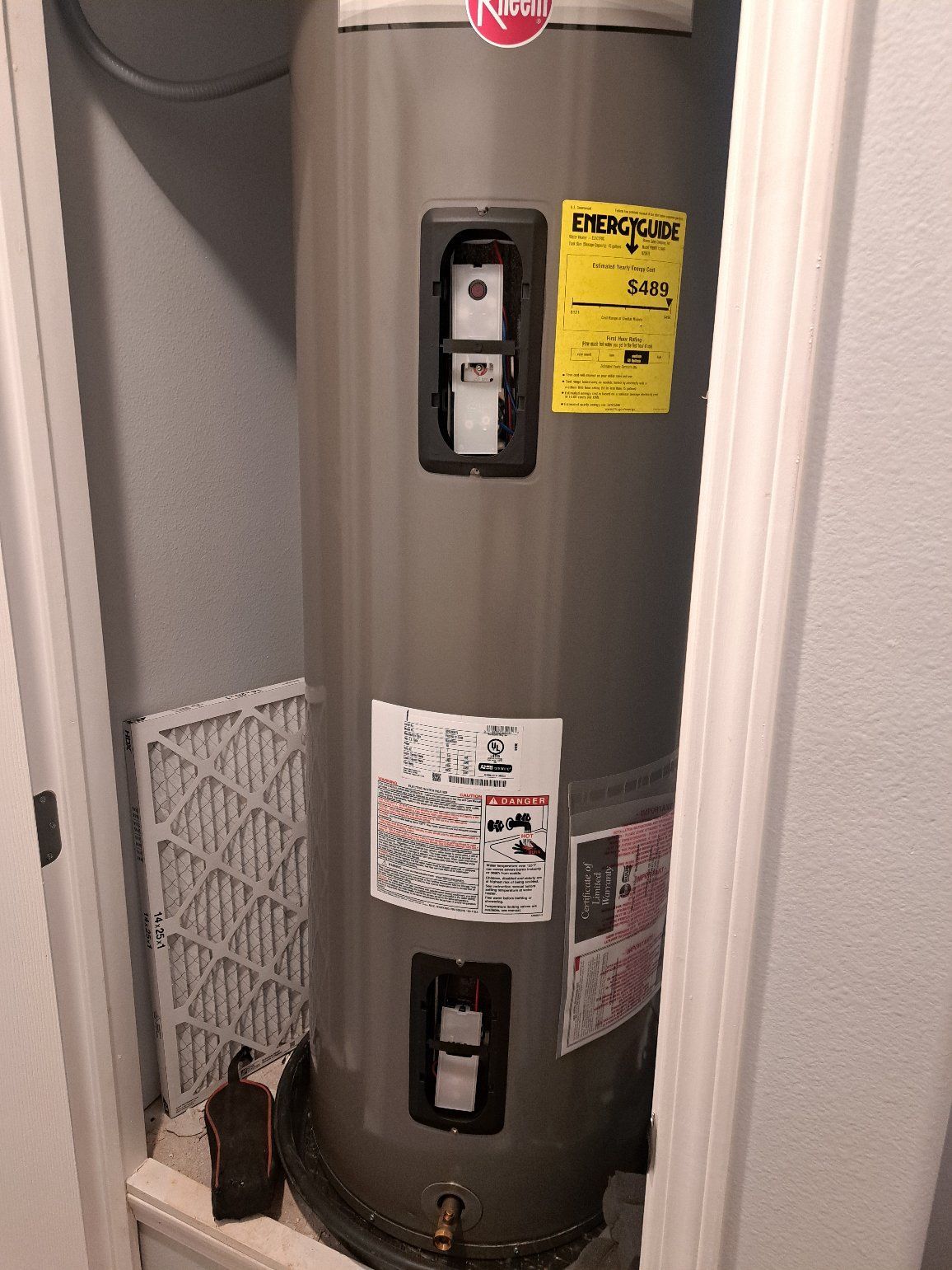 Tall, gray Rheem water heater in a small closet, with an air filter and bottles on the shelf below.