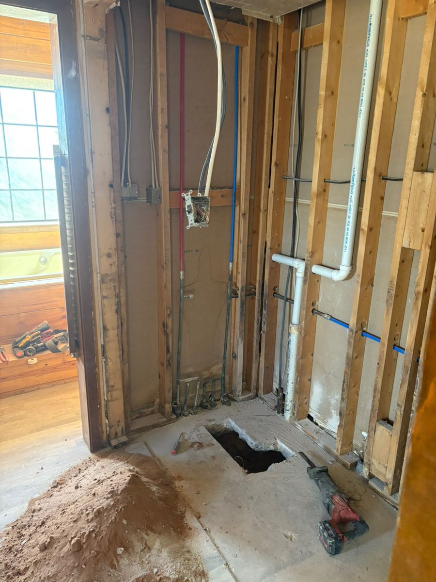 Partially demolished wall framing with exposed plumbing and a floor cutout during home renovation