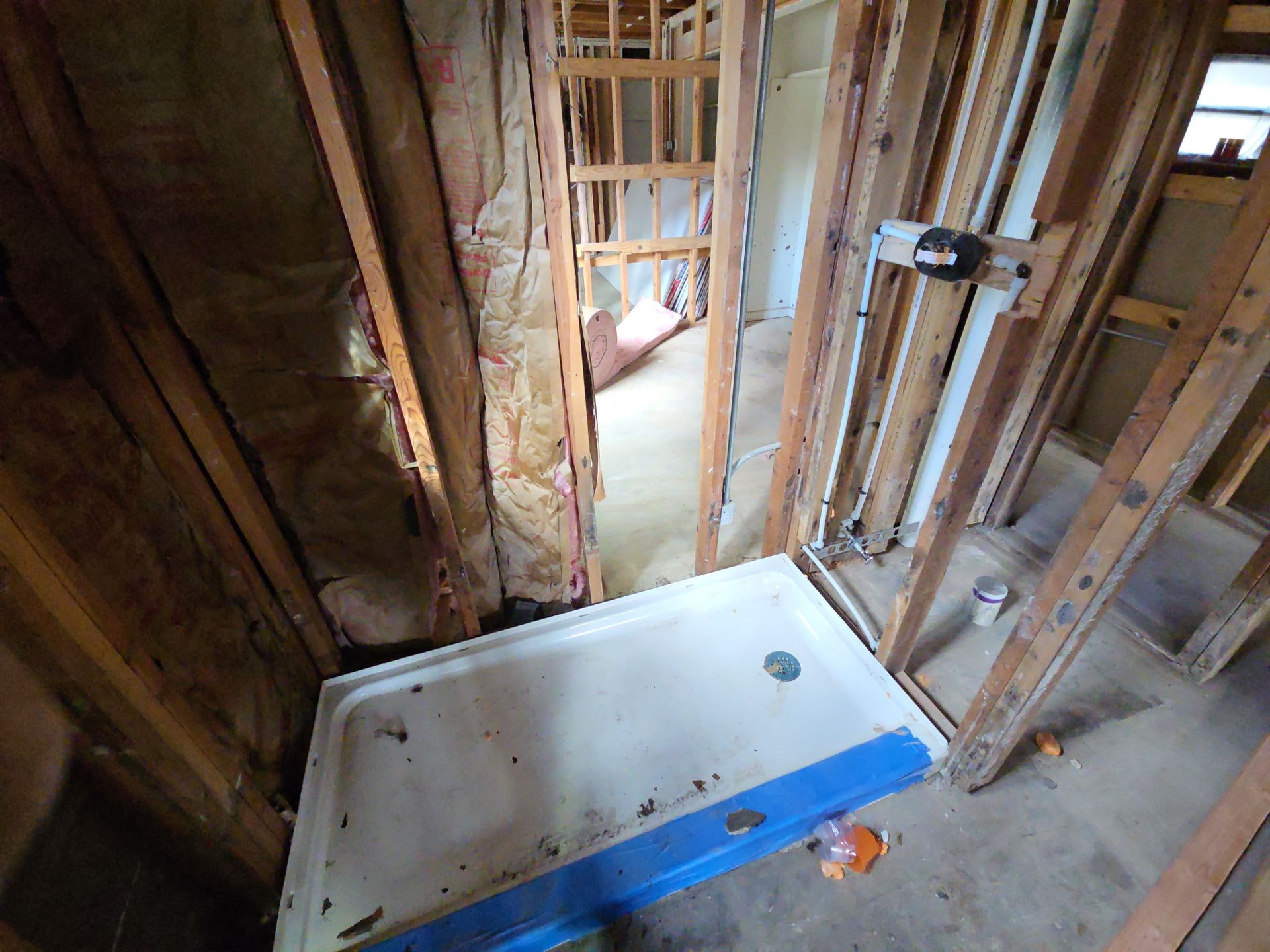 Bathroom under construction with exposed studs and a white tub or shower base on the floor.
