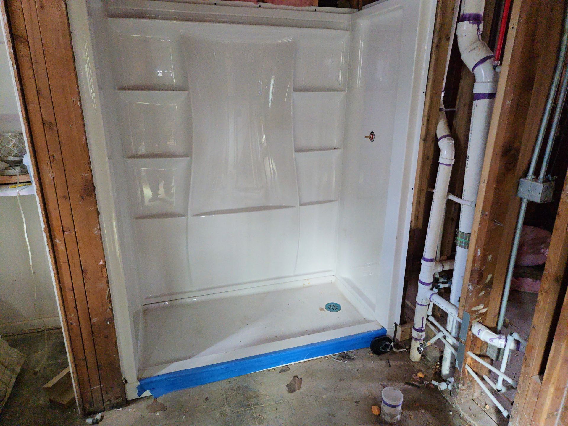 White shower stall under renovation with exposed walls and plumbing on the right