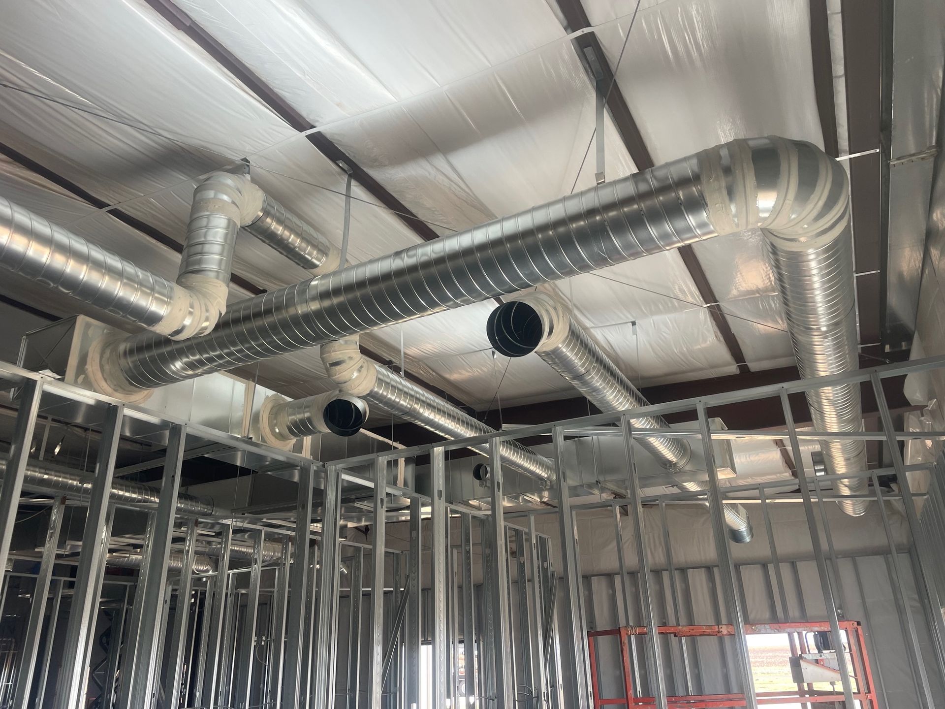 Unfinished building ceiling with exposed metal ductwork, framing, insulation, and a window opening.