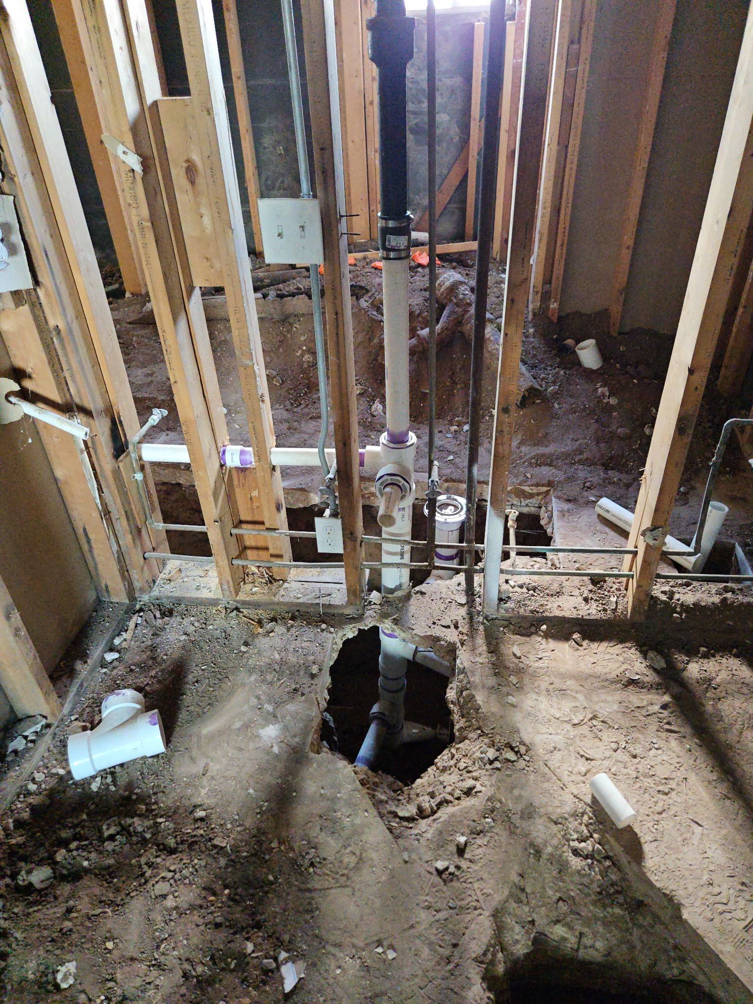 Interior under construction with exposed wooden studs, dirt floor, and a large hole in the center.