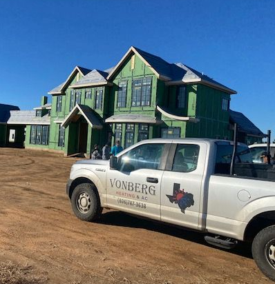 White pickup truck in front of a green house under construction on a dirt lot