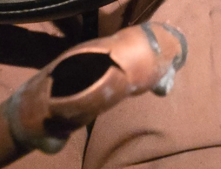 Close-up of a copper-colored metal pipe opening, held by a hand against a brown background