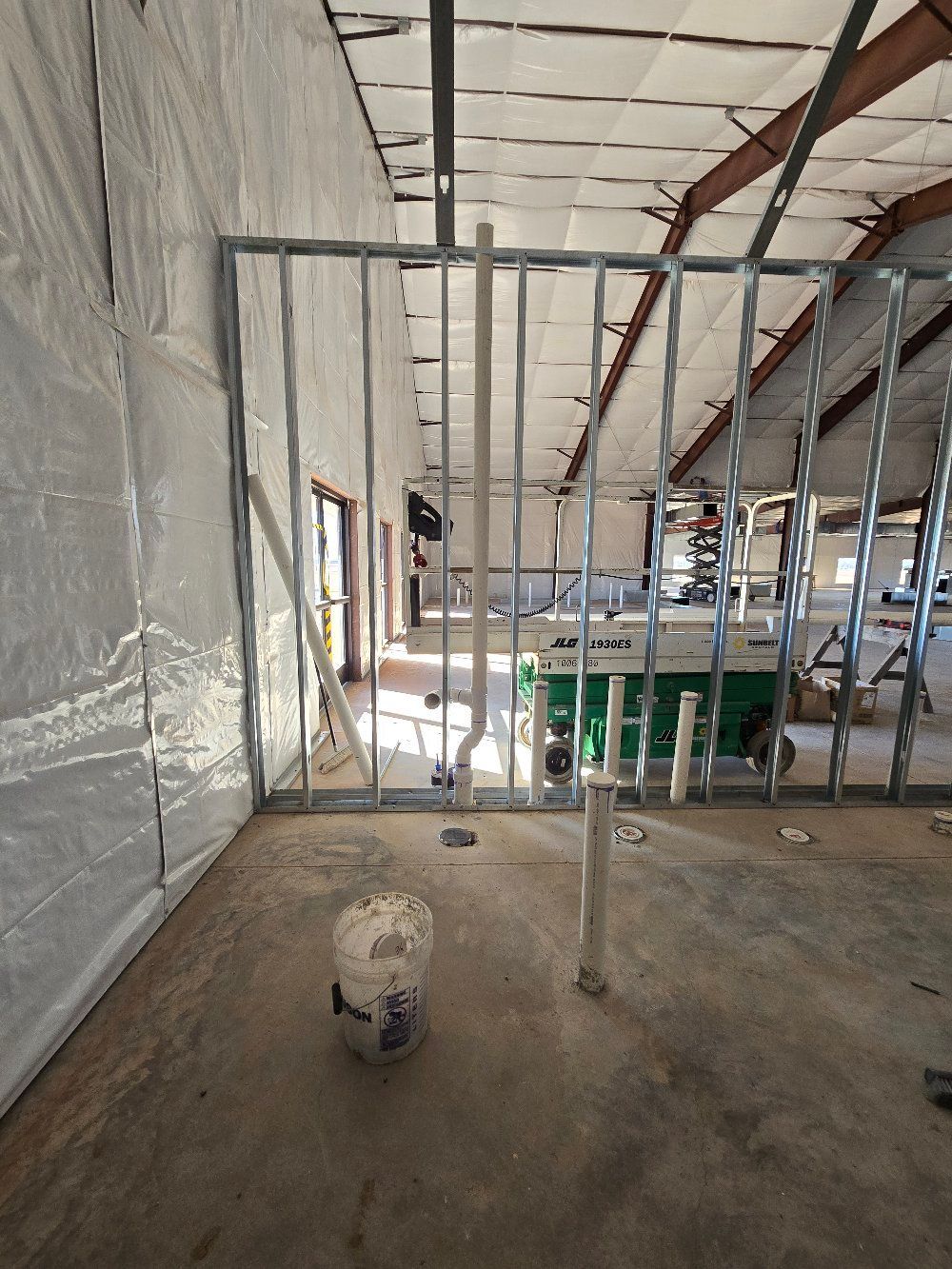 Construction site interior with exposed metal framing, insulation, and scattered materials on a concrete floor.