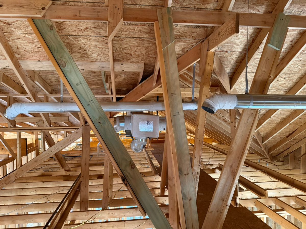 Exposed wooden attic framing with HVAC ducts and support beams under construction