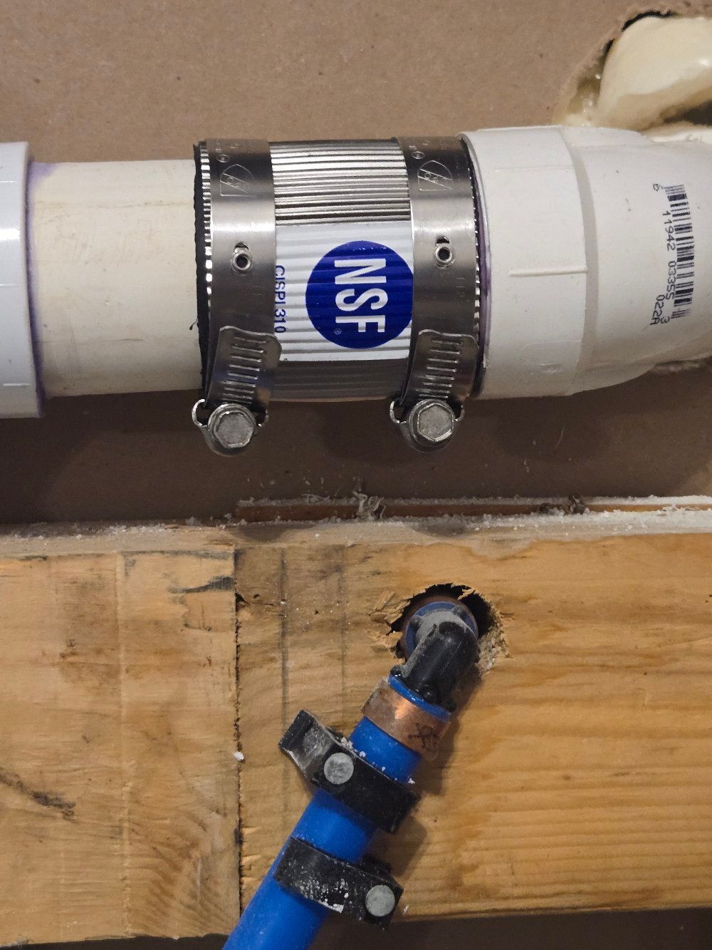 Two connected pipes with metal clamps, one white PVC and one blue fitting, mounted on wood