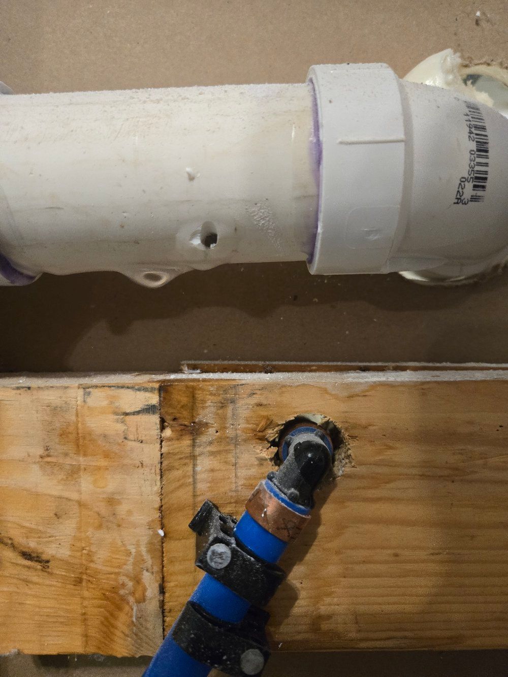 White PVC pipe above a wooden beam, with a blue-and-black angled pipe connector below it.