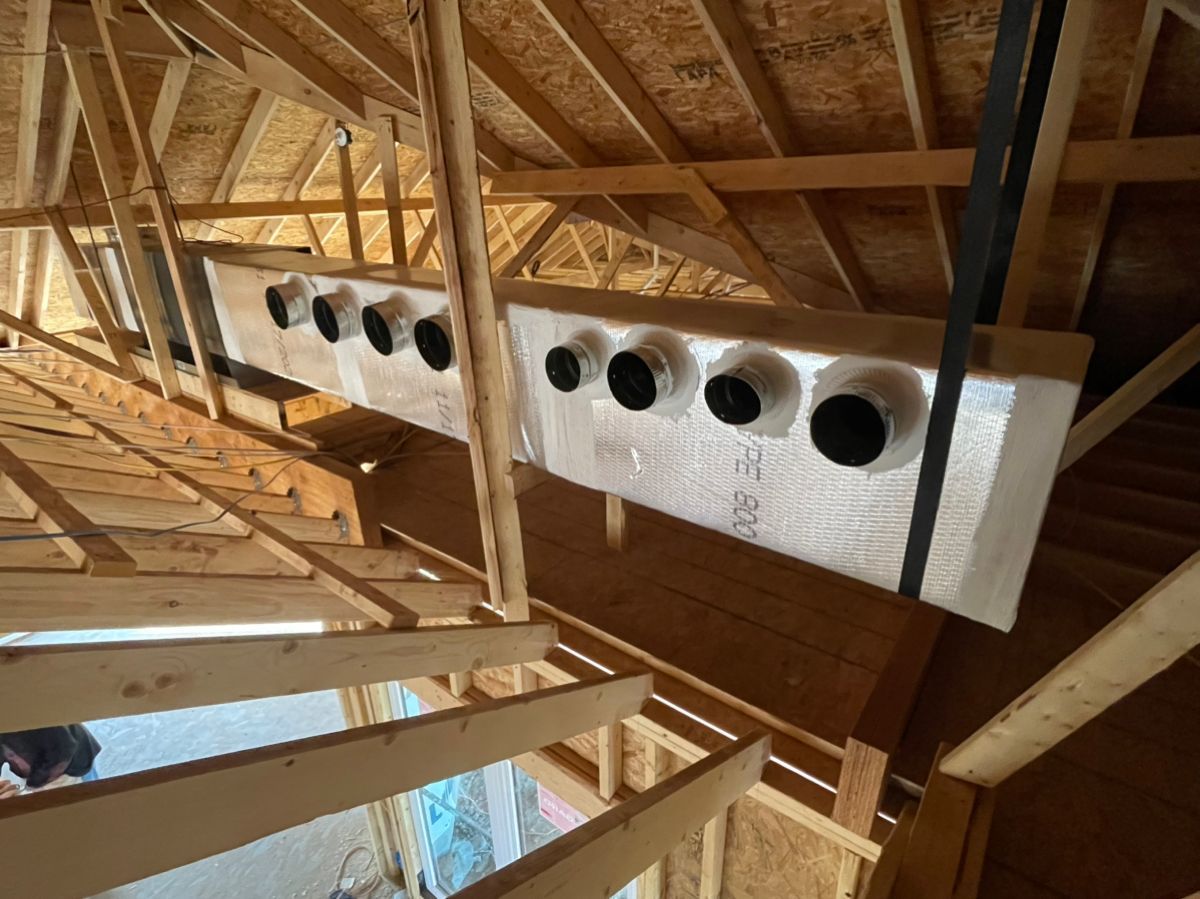 Attic interior with exposed wooden rafters and a long white vent duct with circular openings