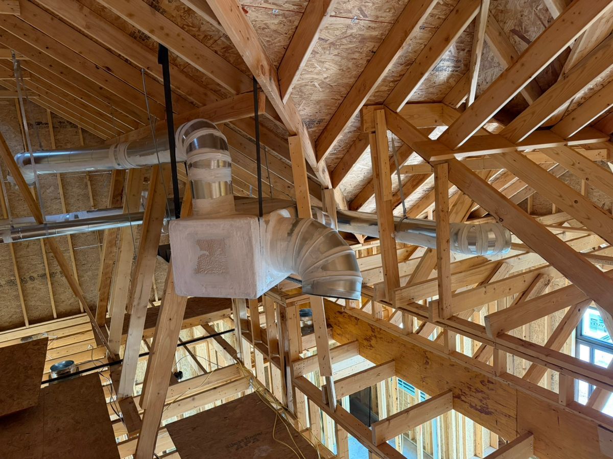White HVAC ductwork suspended among exposed wooden roof trusses in an attic-like space
