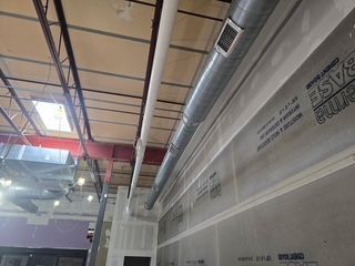 Indoor industrial warehouse ceiling with exposed beams, ductwork, and a large translucent plastic-covered wall