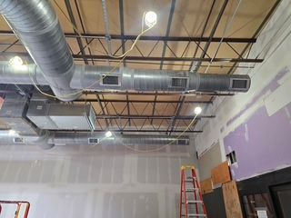 Ceiling ductwork and exposed rafters in an unfinished room with a red ladder against the wall.