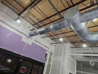 Industrial ceiling with exposed ductwork, lights, and unfinished purple-and-white walls in a room under construction