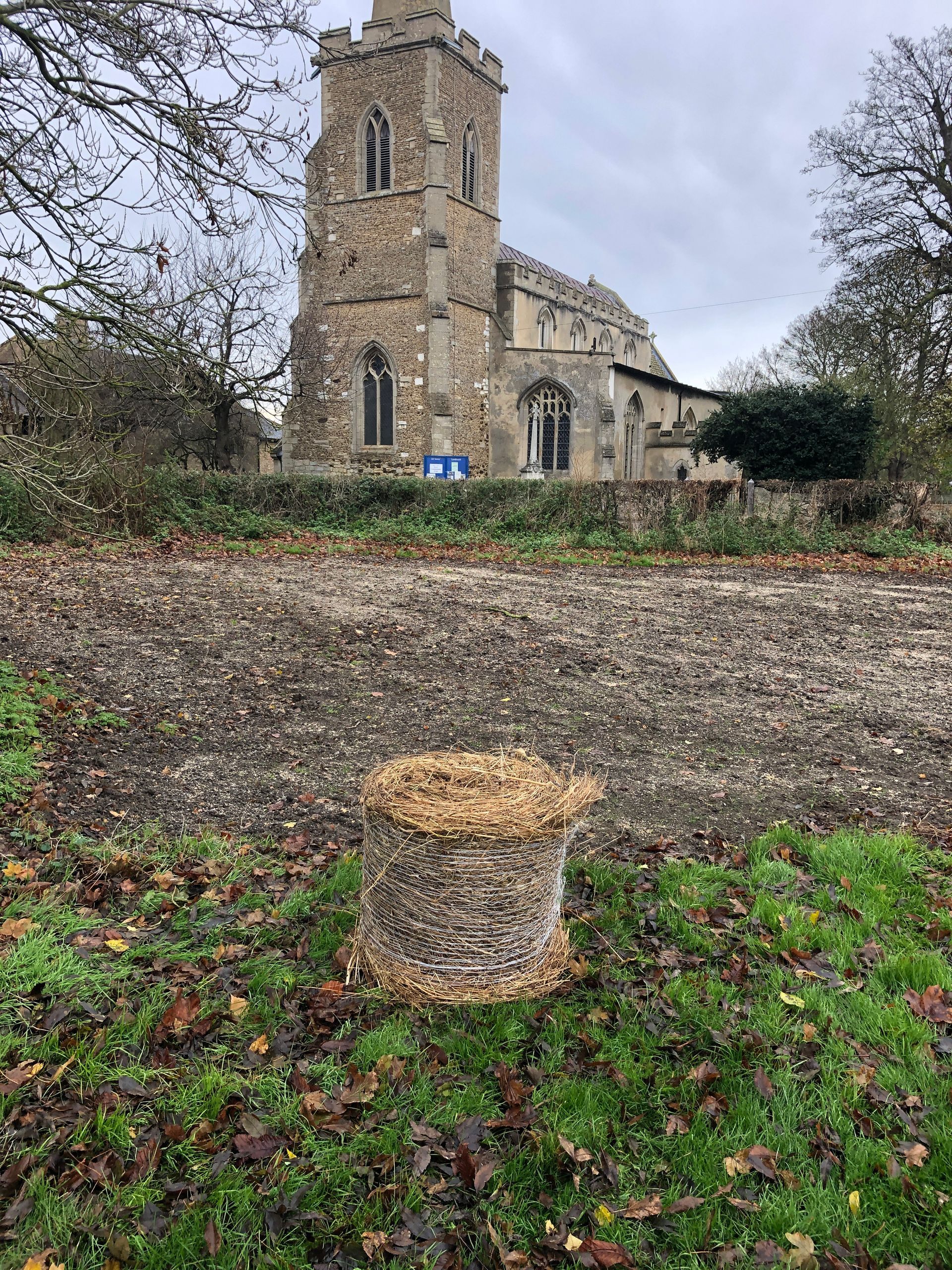 A pile of hay is sitting in a field in front of a church.