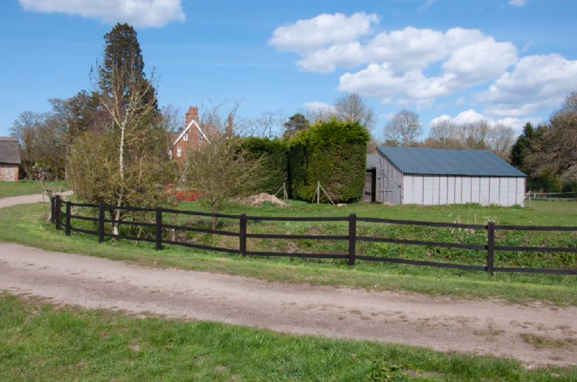 A fence surrounds a grassy field with a barn in the background.