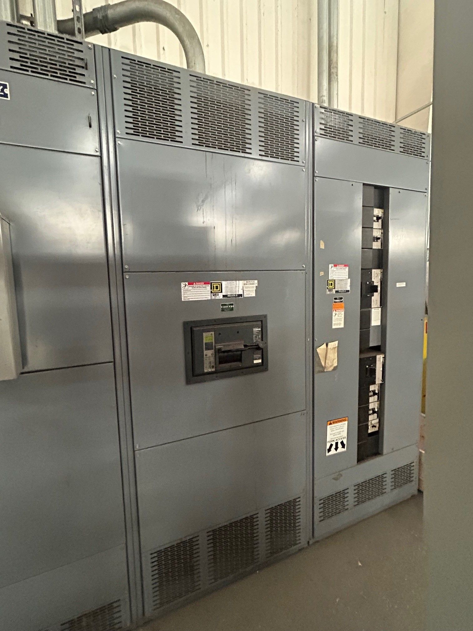 Gray electrical panel with grates, warning labels, and a circuit breaker.