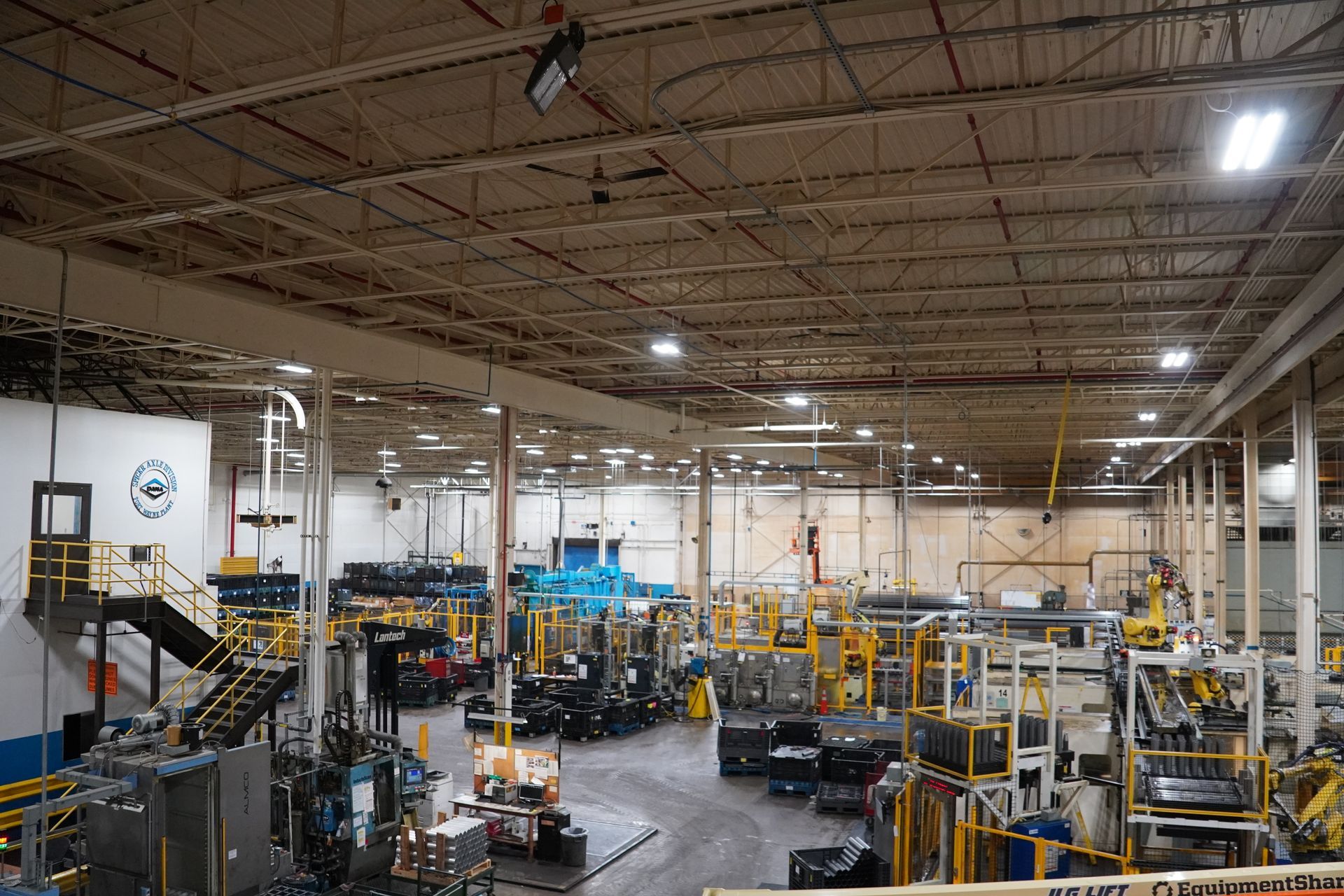 Two workers inspecting machinery, one holding circuit board, other with screwdriver. Industrial setting.