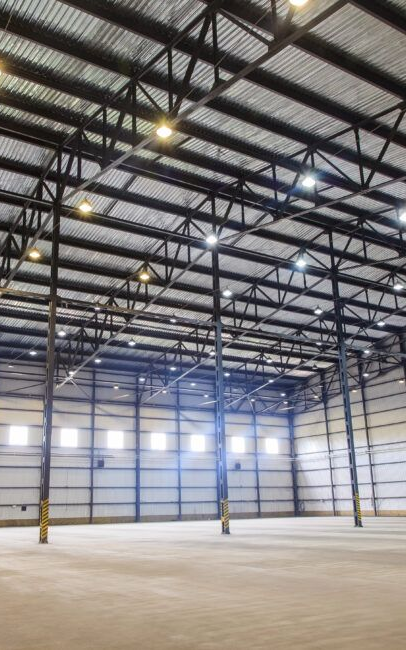 Interior of a large, empty warehouse with metal beams, support columns, and ceiling lights.