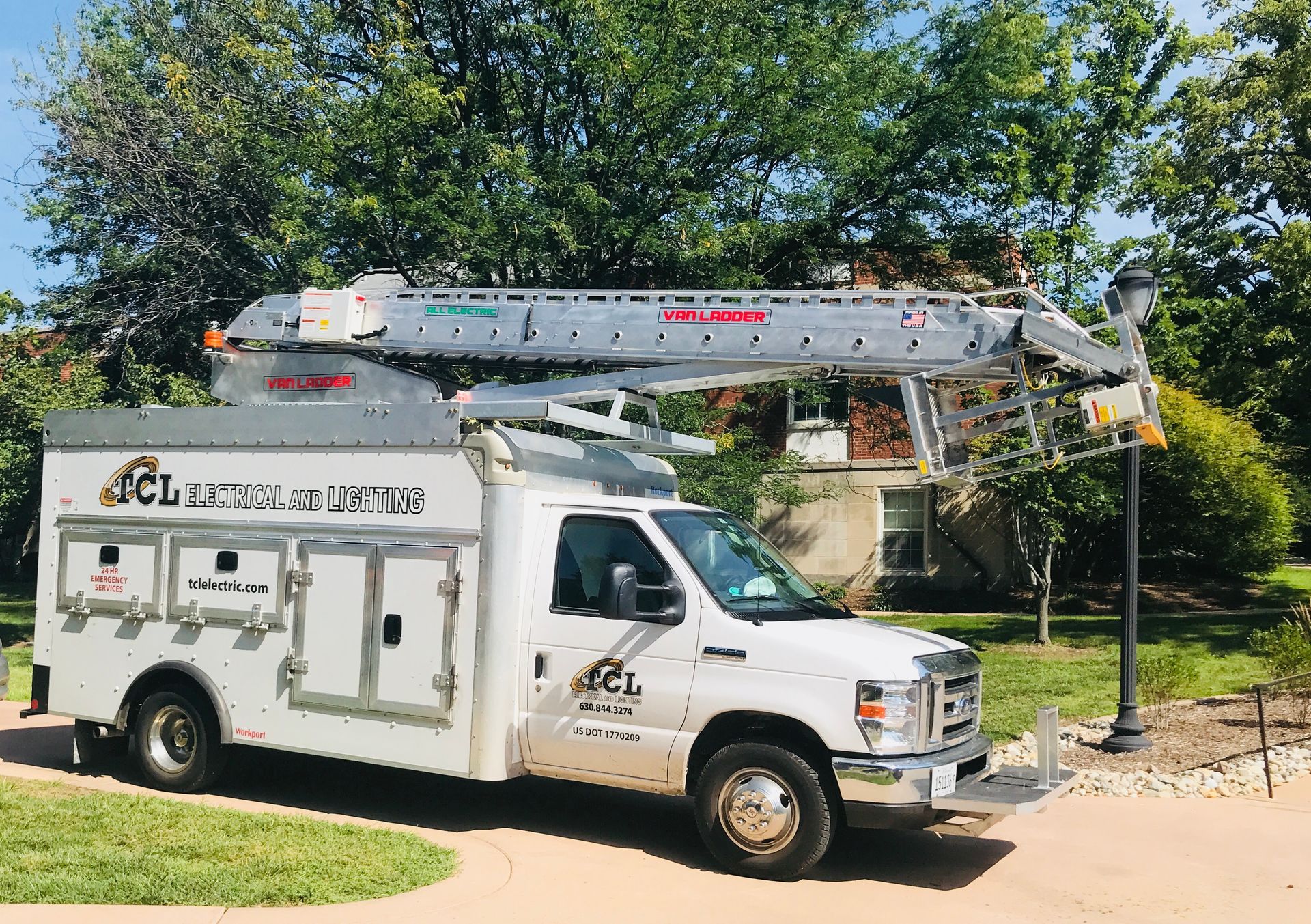 White utility truck with an aerial lift parked on a grassy area near a house.
