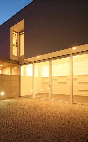 Modern building exterior at dusk, glass doors open to illuminated interior, brick paving.