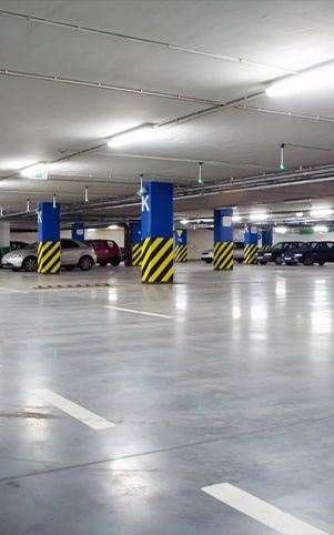 Indoor parking garage with concrete floor, cars parked, blue and yellow support columns, and fluorescent lights.
