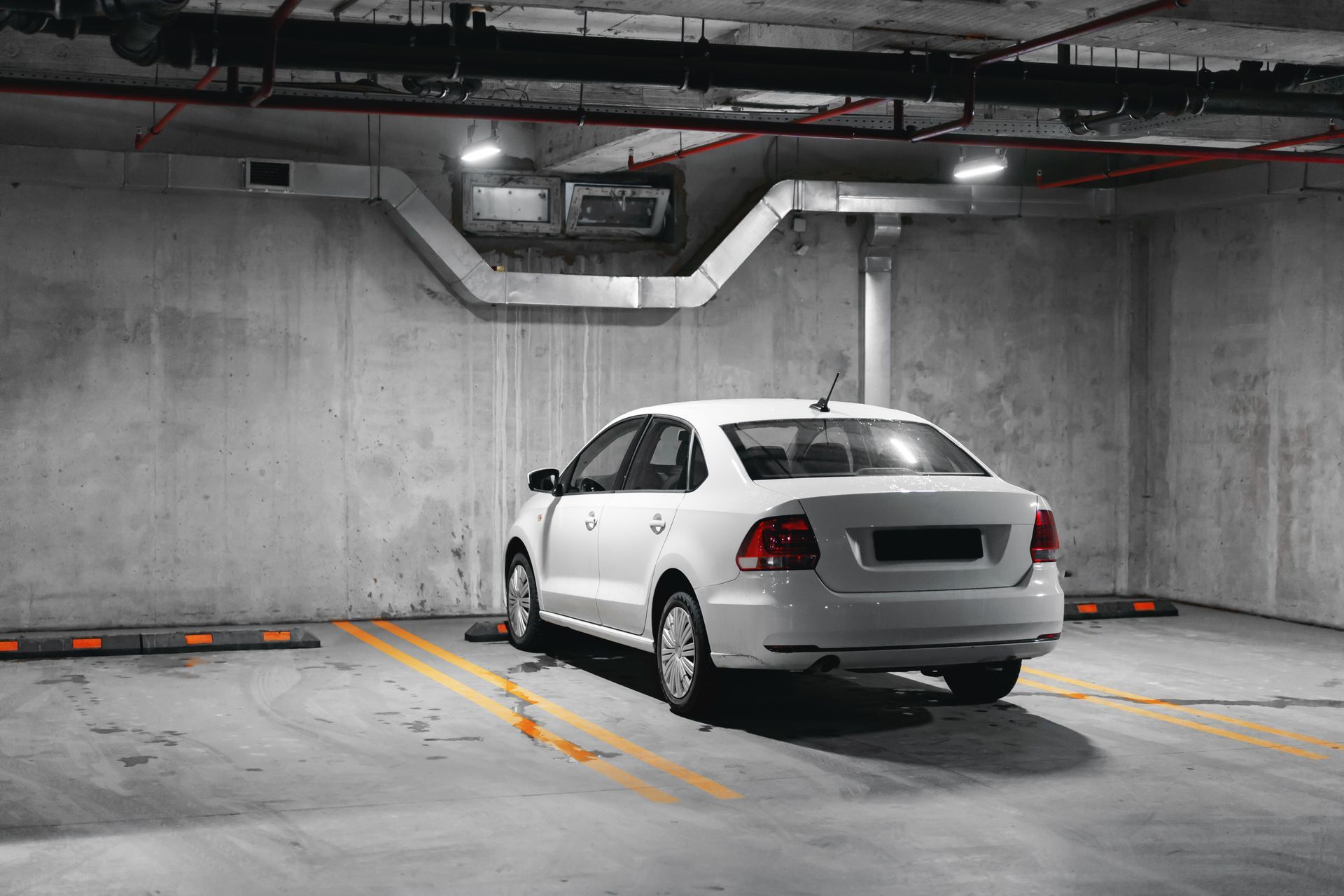 White car parked in an underground parking garage with yellow parking lines on the concrete floor.
