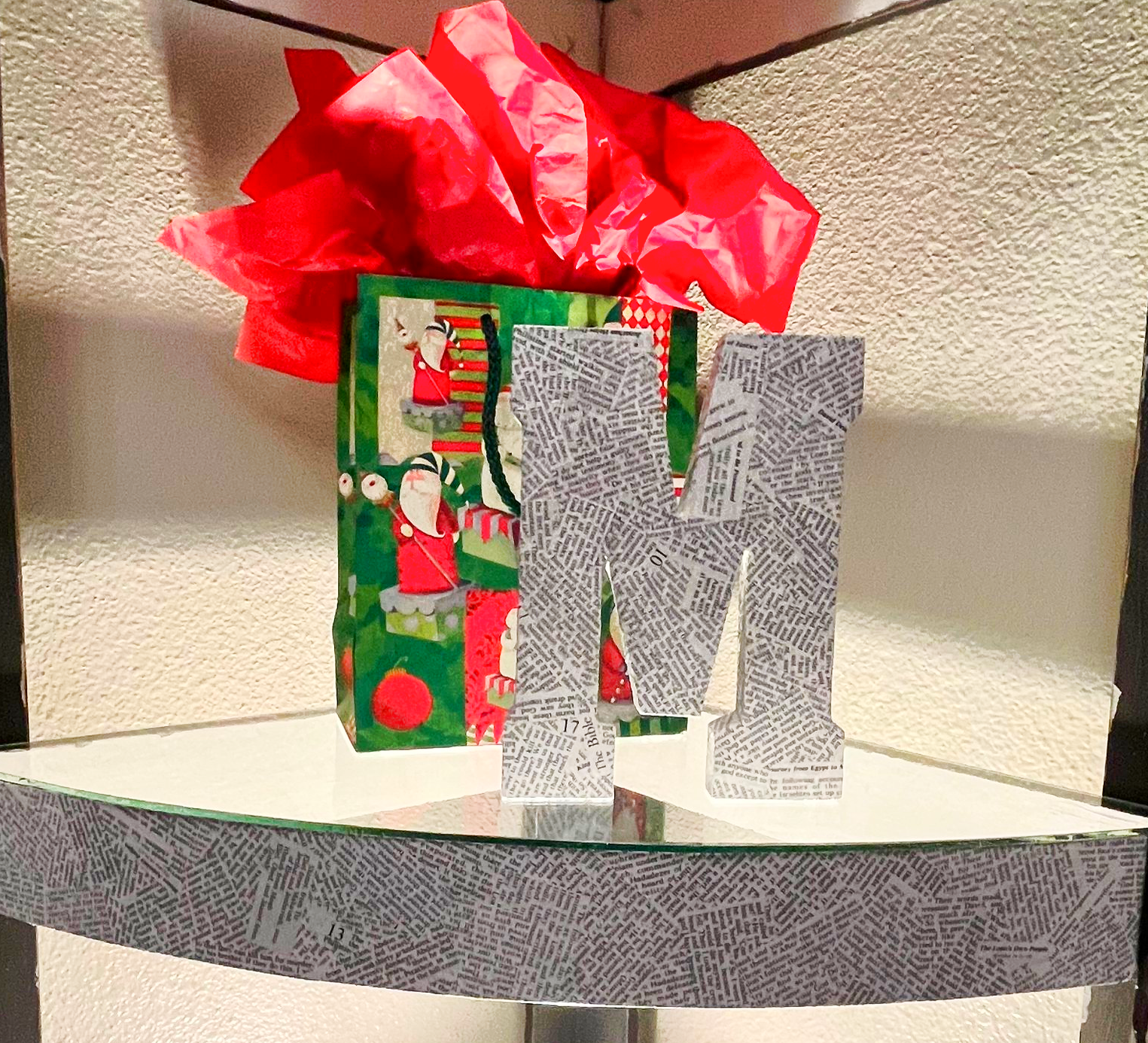 Decorative gift box with a red bow and a patterned letter M on a shelf