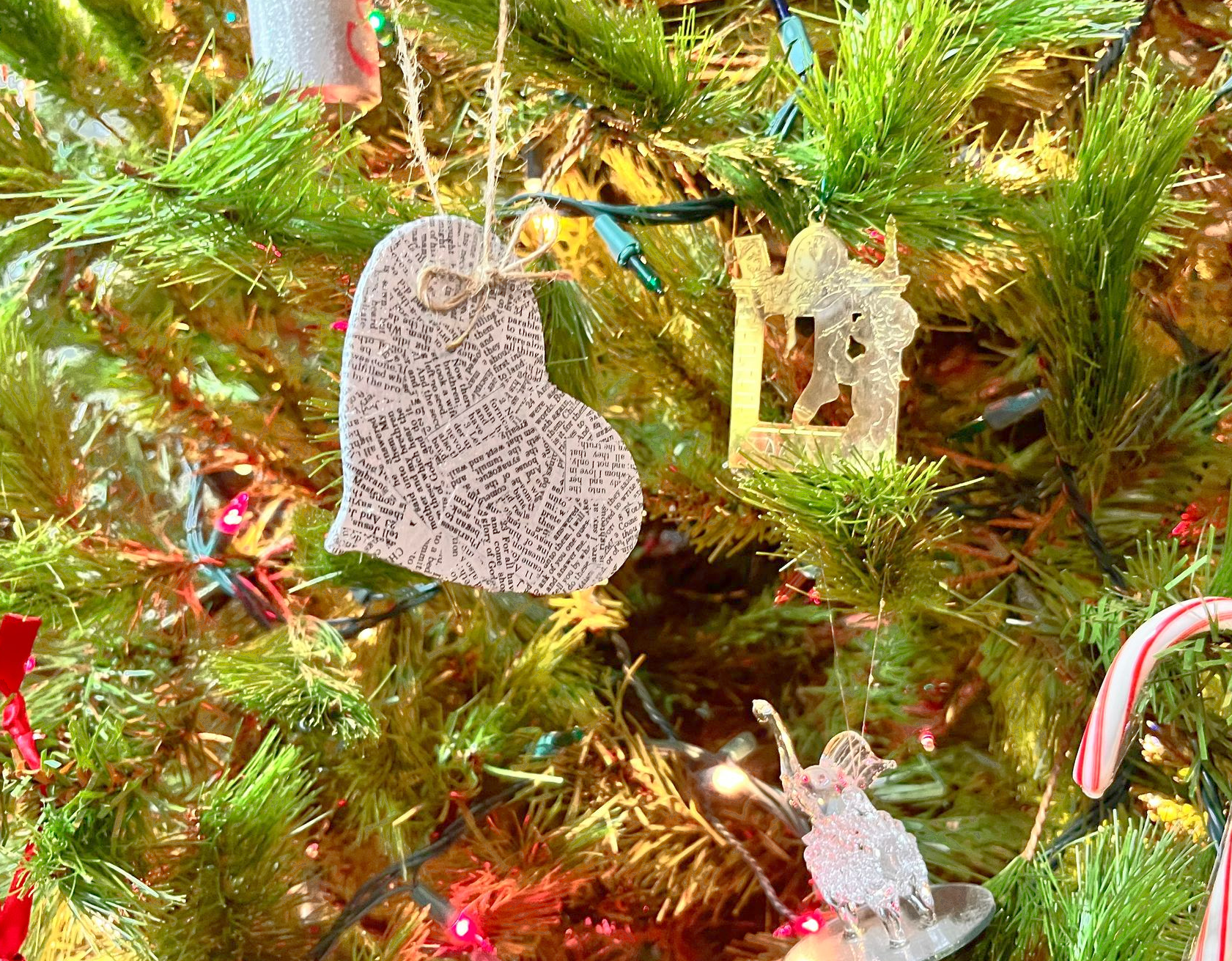 A decorated Christmas tree with gold tinsel and hanging ornaments, including a speckled heart and angel.
