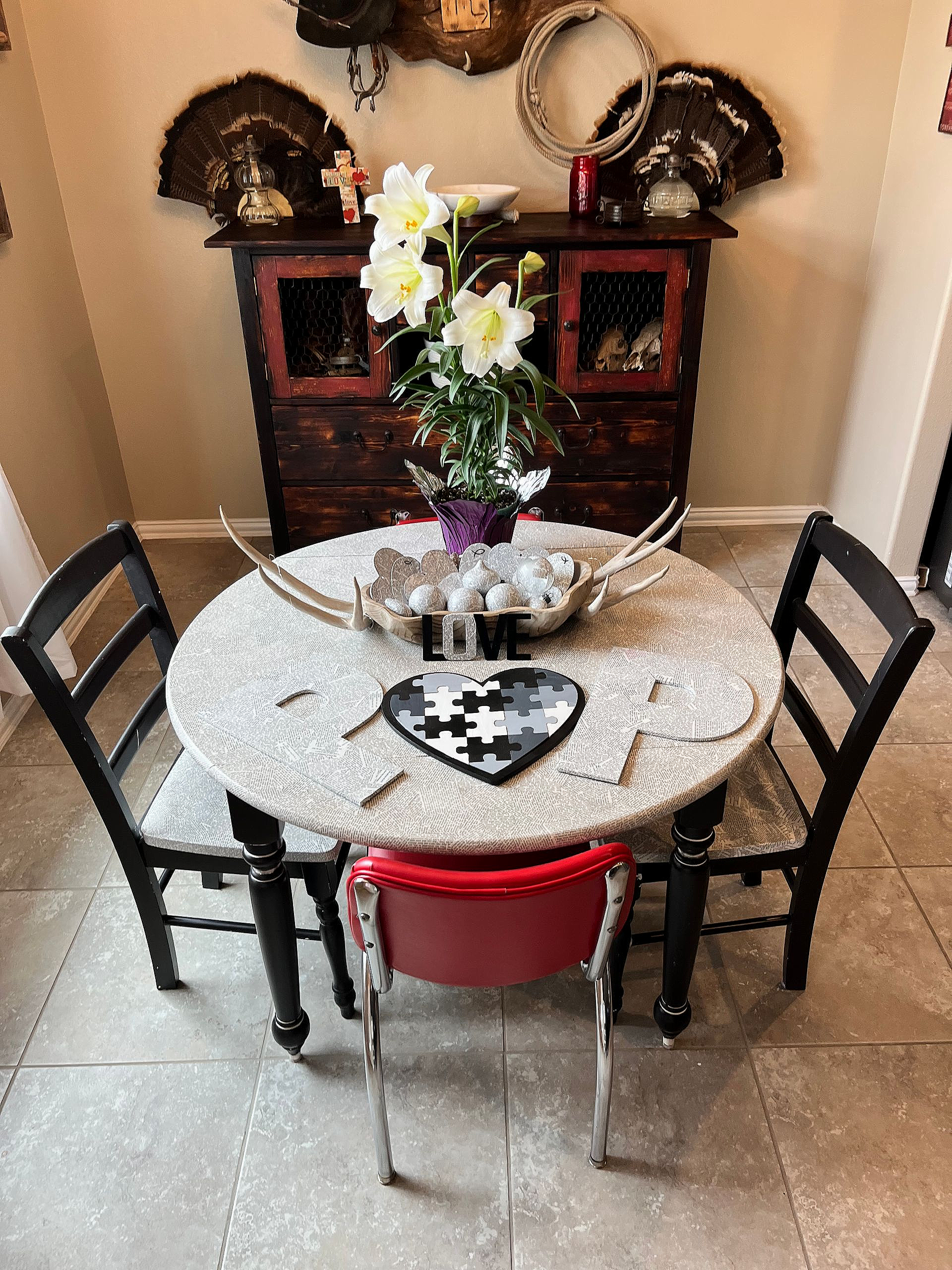 Round dining table with lace cloth, floral centerpiece, black chairs, and a red chair in a cozy room