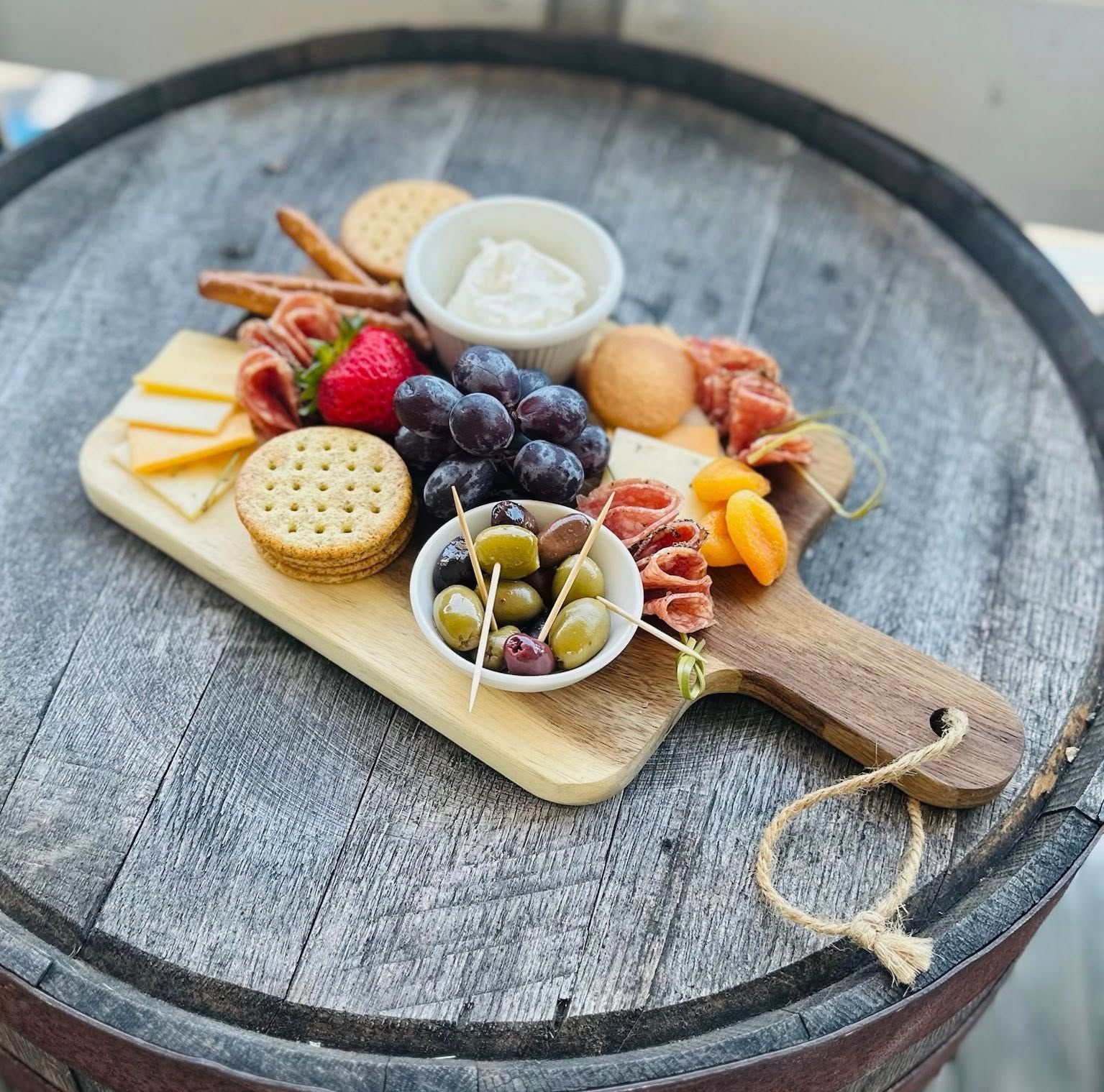 Charcuterie board on a wooden barrel with crackers, cheese, grapes, olives, and dip.