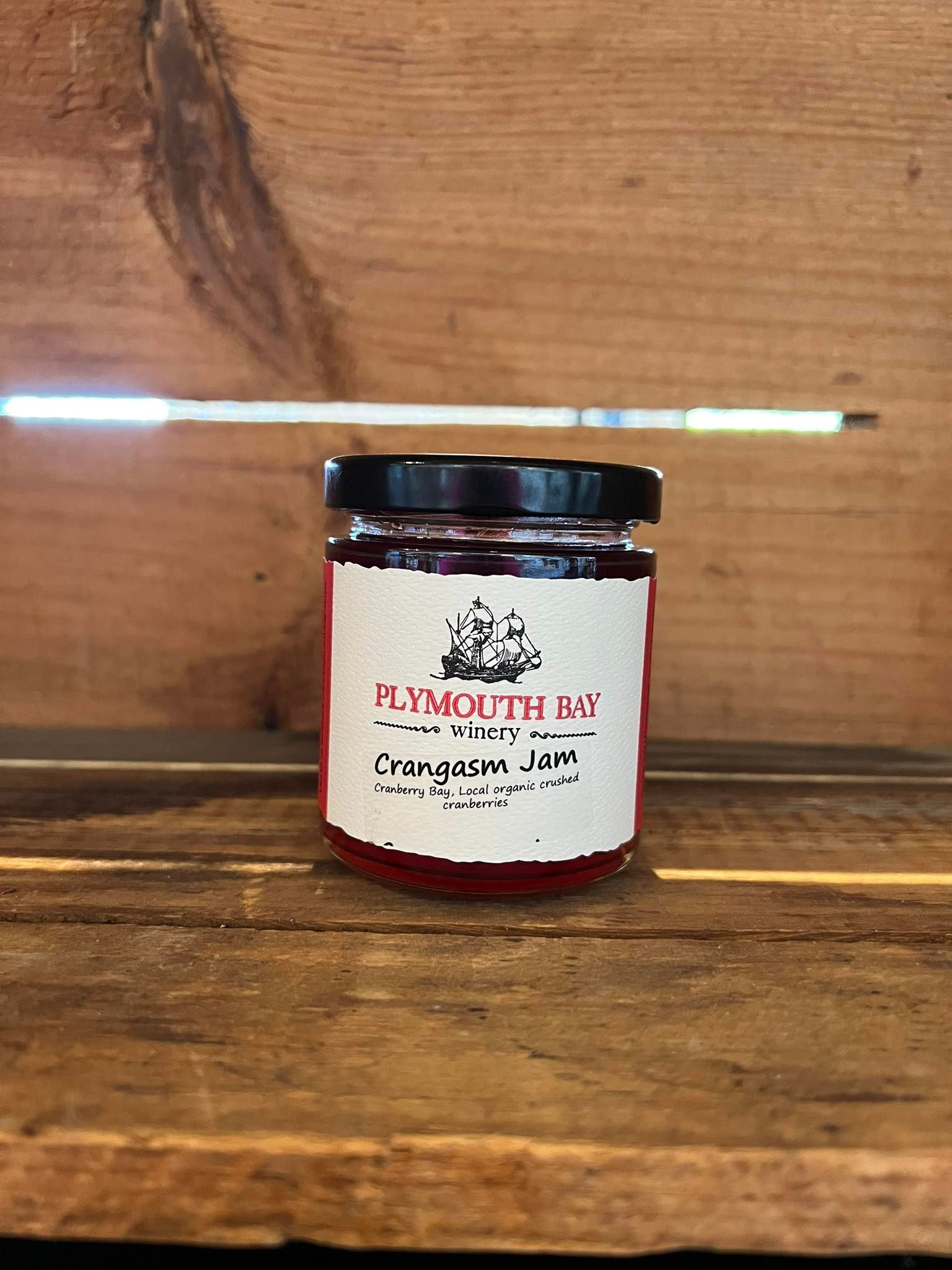 Jar of Plymouth Bay Cranberry Jam on a wooden surface, with a wooden background.