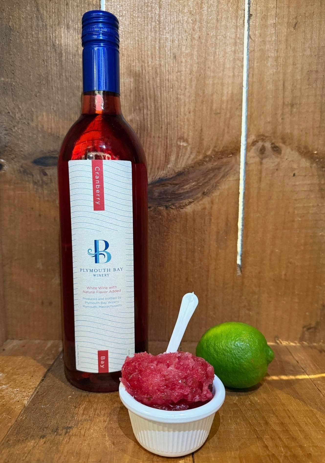 Bottle of red wine, pink slushy, and lime on a wooden surface.