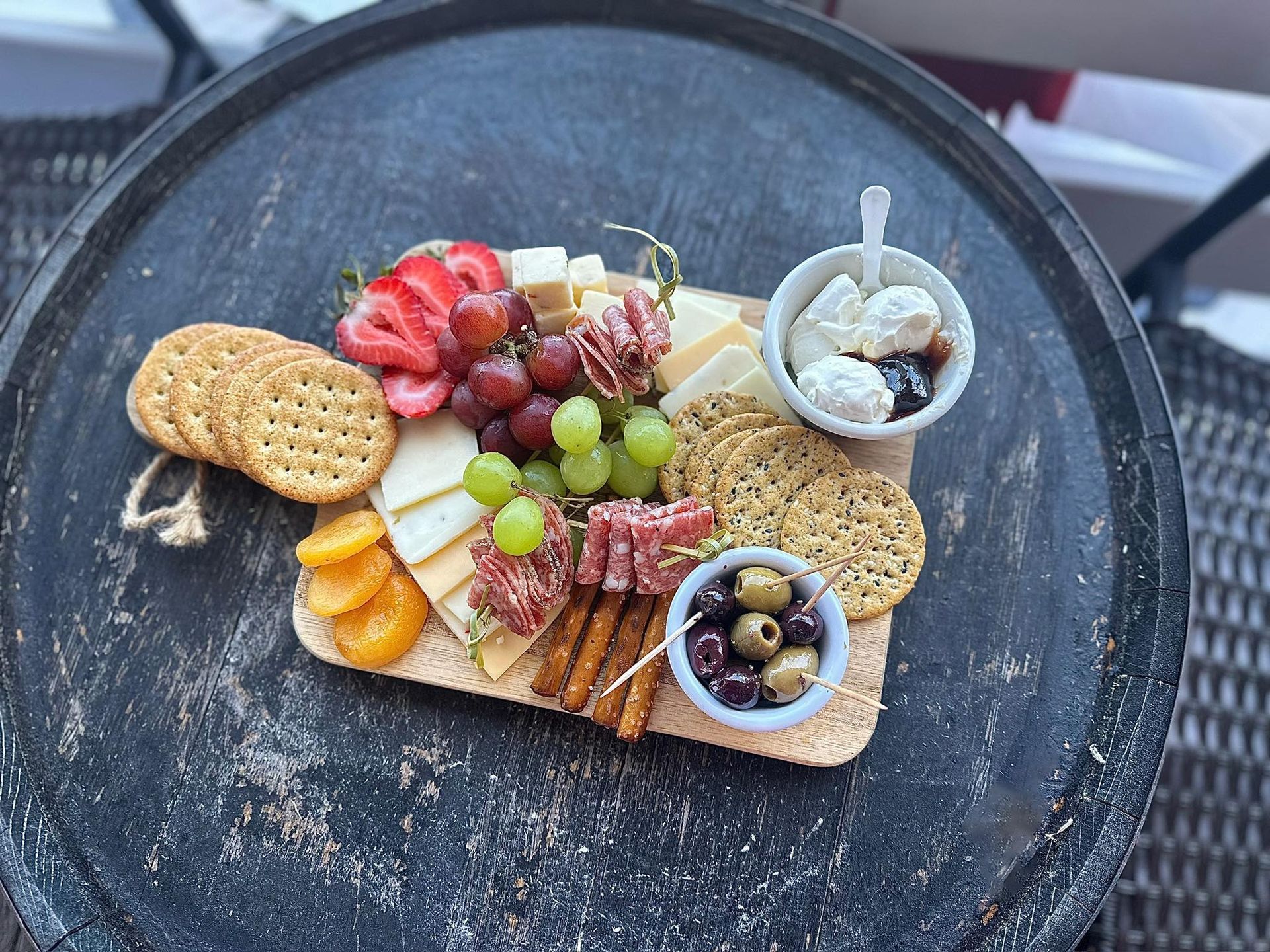 Charcuterie board on a round table, with crackers, cheeses, fruits, meats, olives, and a dip.