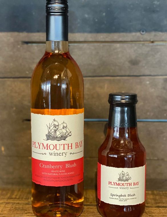 Two bottles of Plymouth Bay Winery Cranberry Blush and Sparkling Blush on a wooden surface.