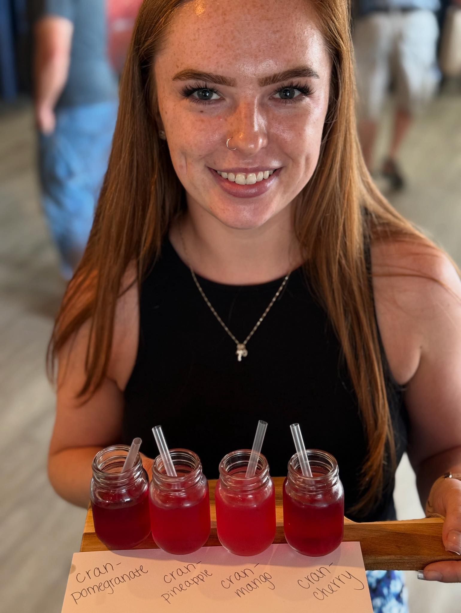 Woman holding tray of red drinks; indoors, smiling.