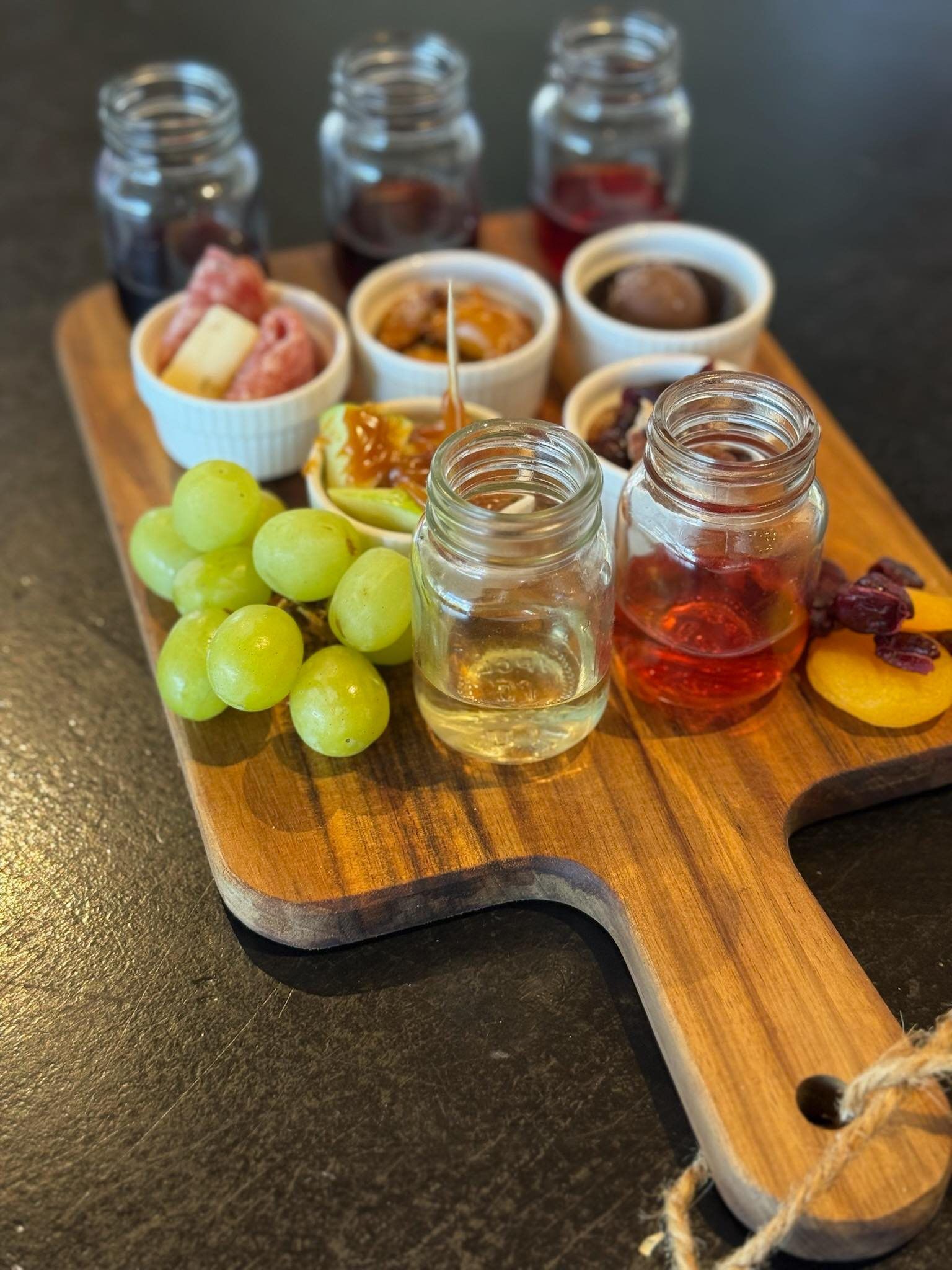 Wooden charcuterie board with jars of liquids and small food dishes, grapes, and a peach.
