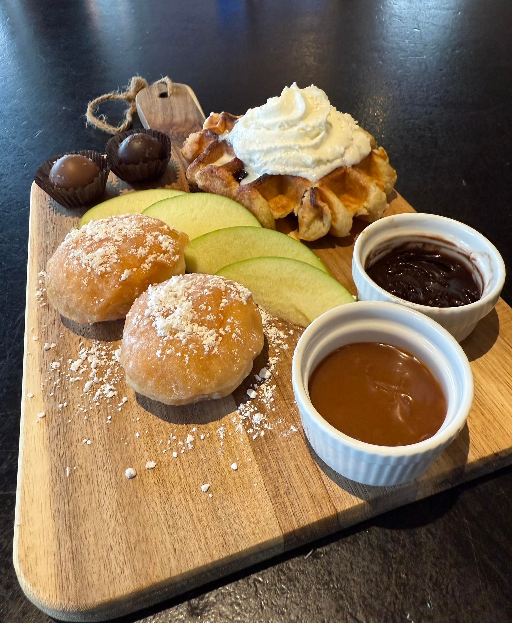 Dessert platter: waffle with whipped cream, donuts, apple slices, chocolate, and dipping sauces.