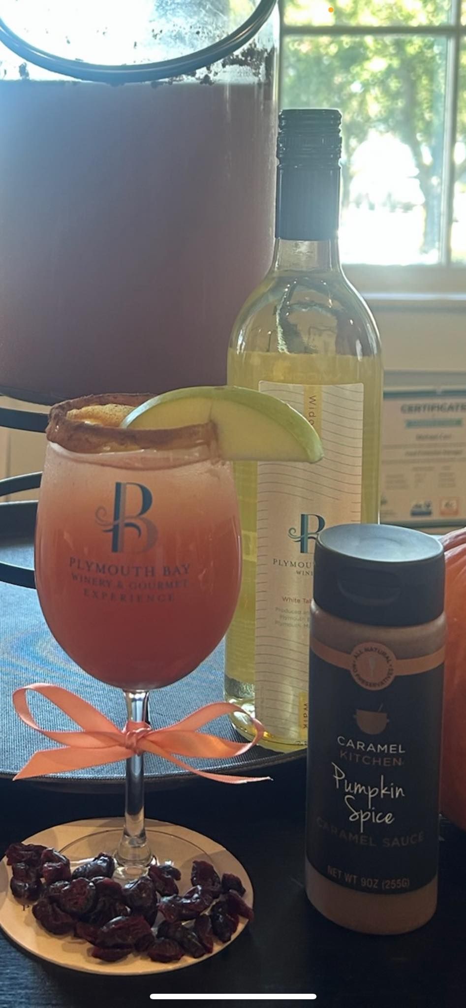 Cocktail with cinnamon rim and ribbon, alongside spice bottle, wine, and cranberry plate.